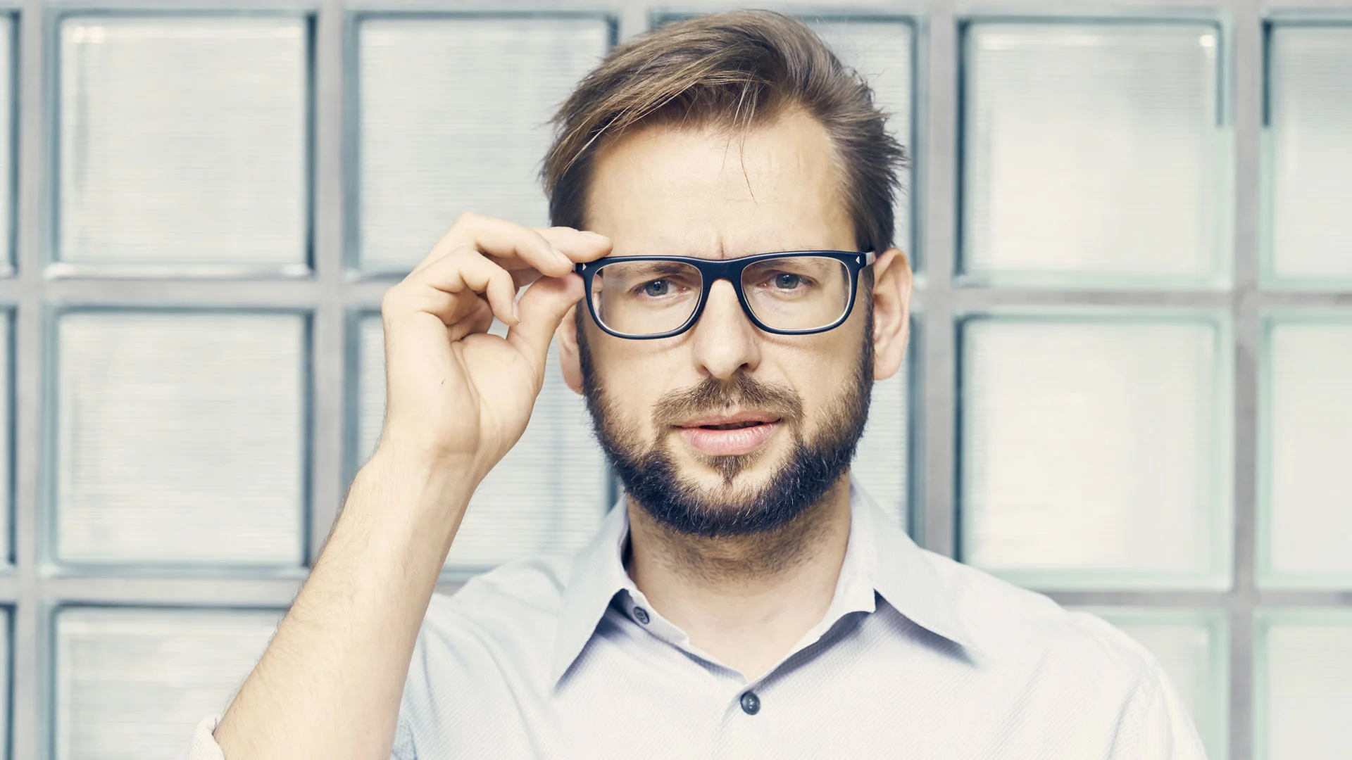 Man adjusting his glasses and lookign confused.