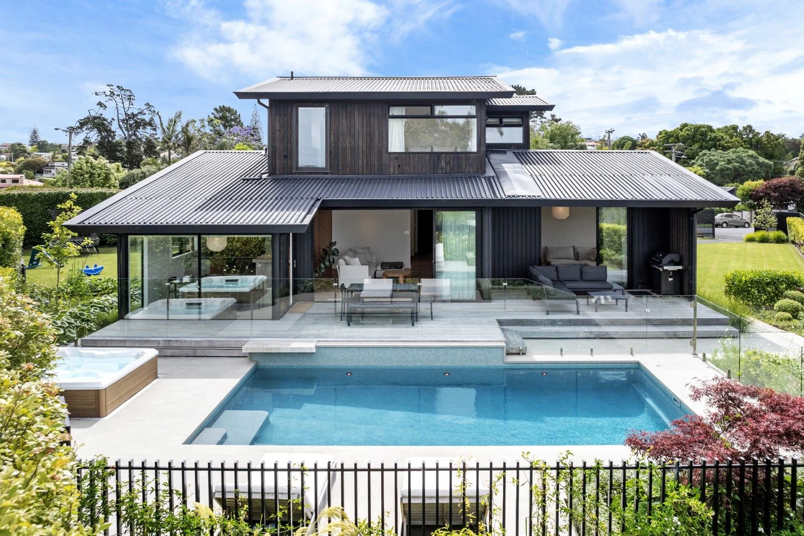 A modern house with a large pool and jacuzzi set out the back. The windows are floor to ceiling letting in lots of light. 