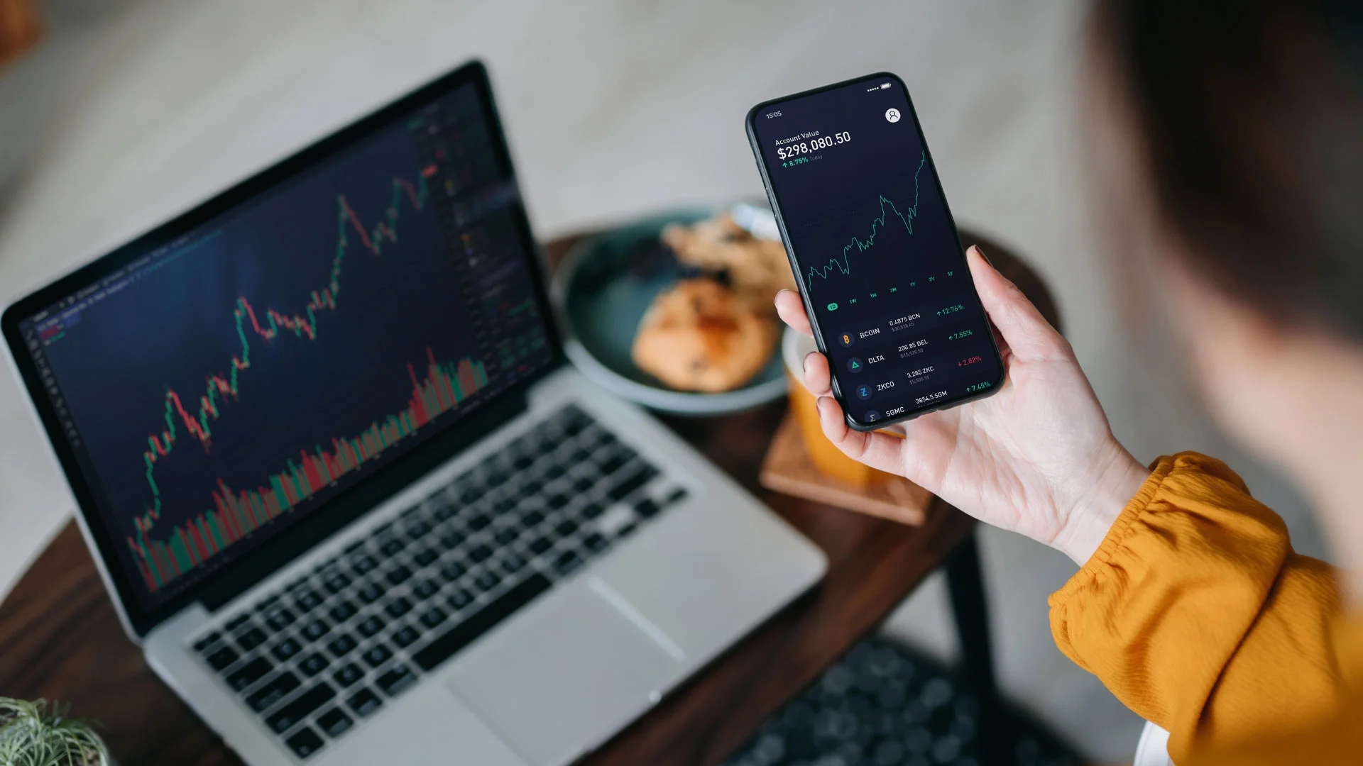 A financial analyst looking at trend graphs on a phone and laptop.