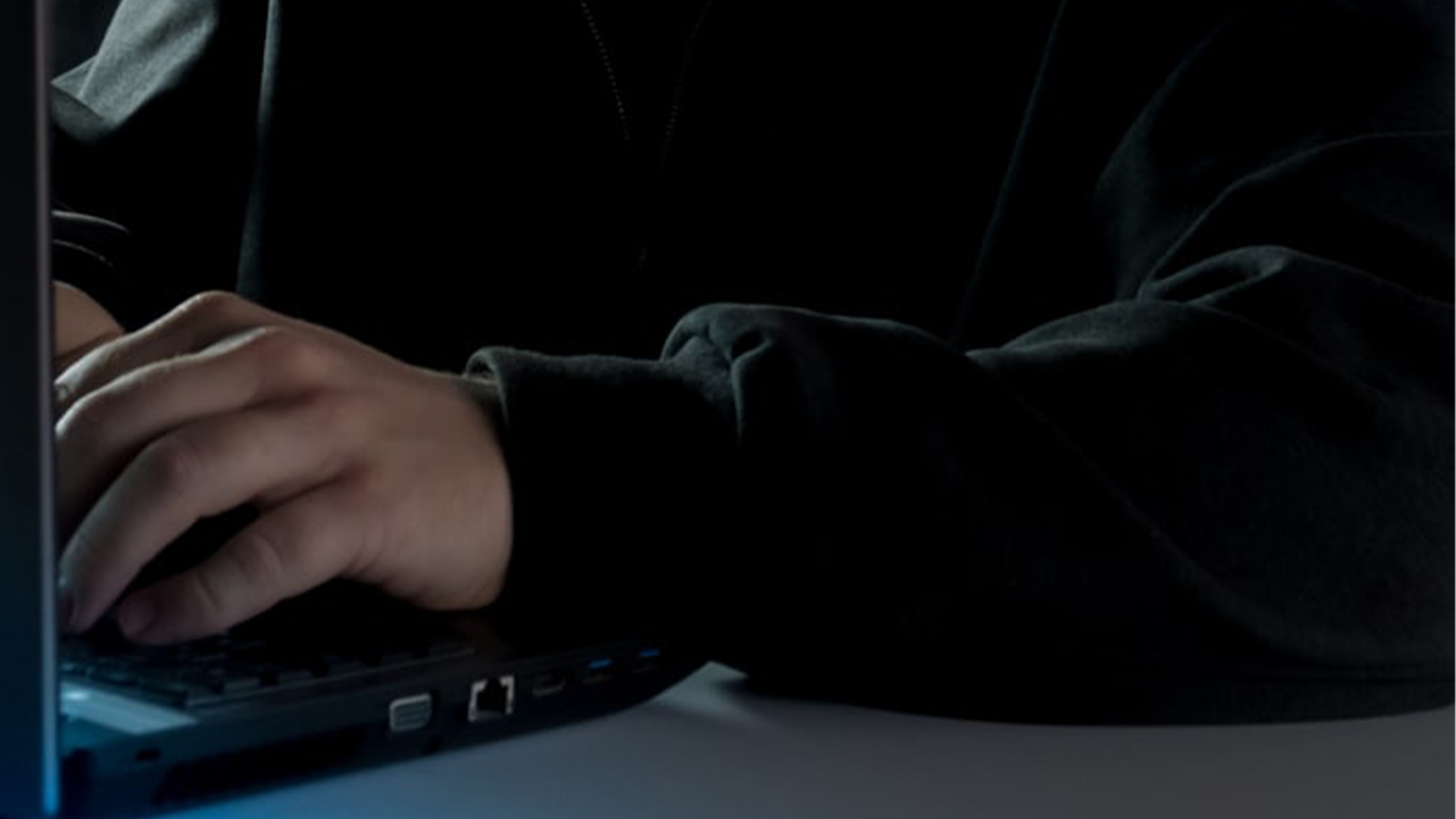 A hooded figure behind a laptop