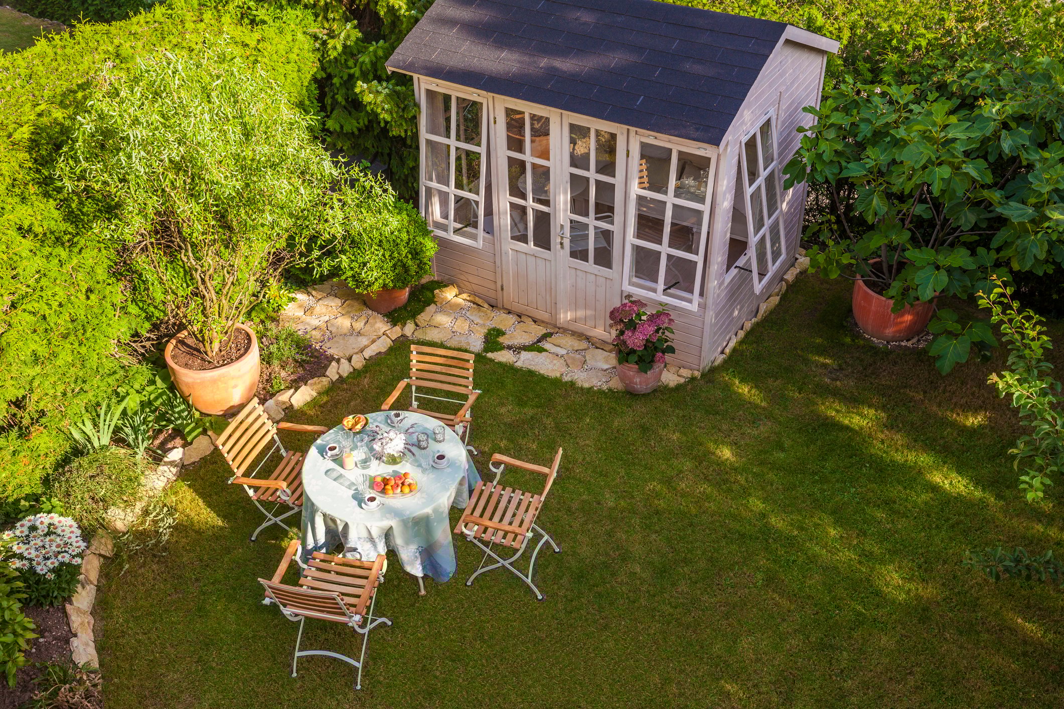 A rustic timber garden shed with a window and a shingle roof, surrounded by green trees and plants in a New Zealand backyard.