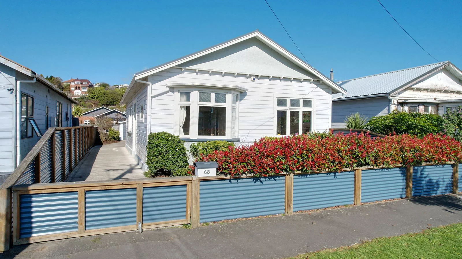 White weather board home with a red and green hedge