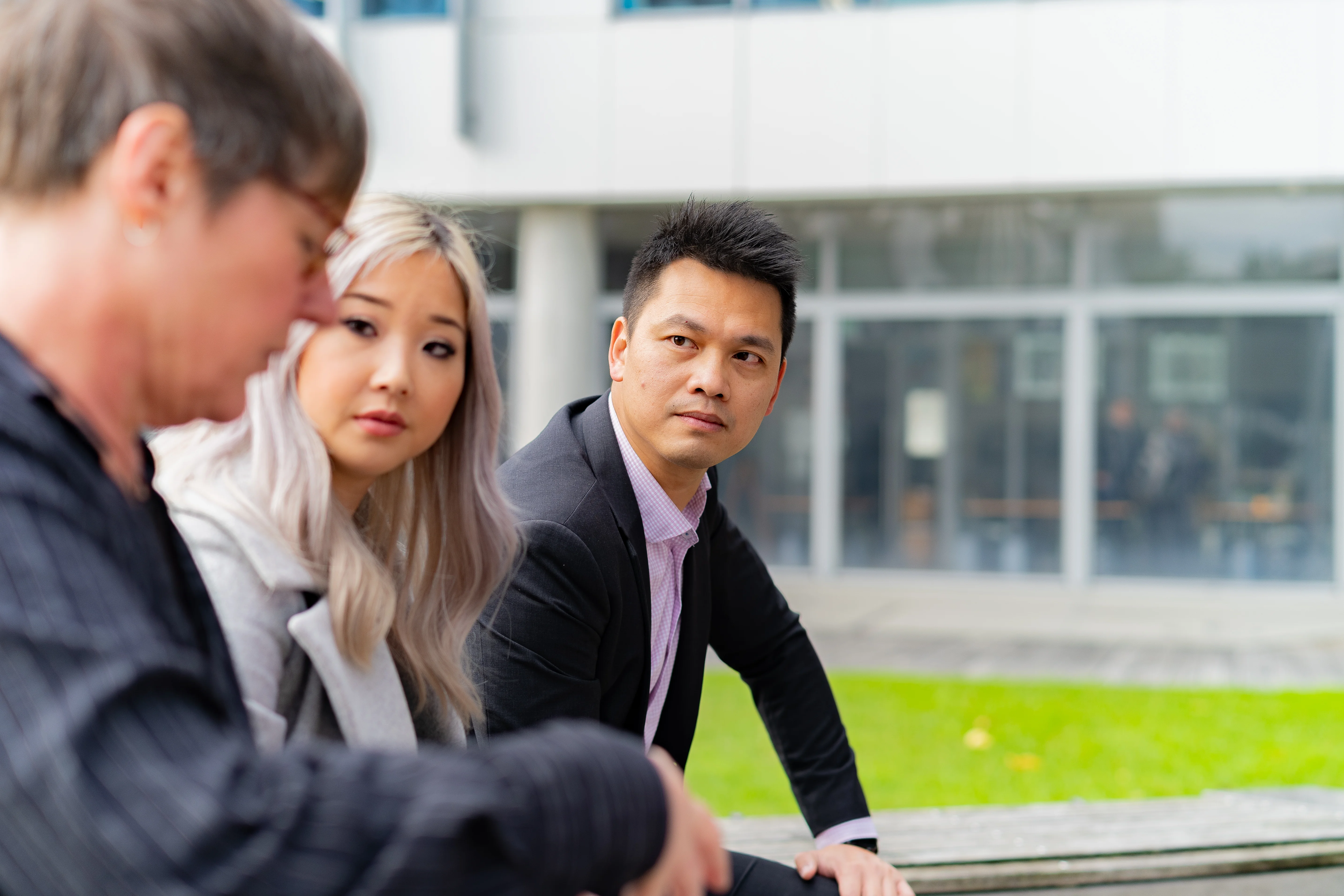 Three people talking outside on a bench.