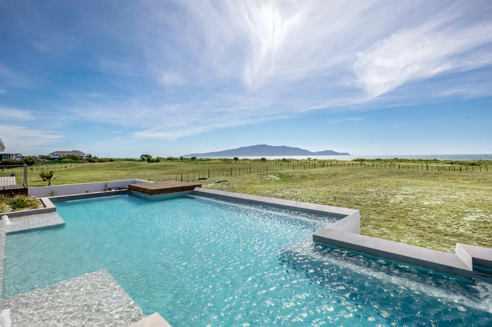 Large clear pool in the foreground with the sea and mountains in the back. 