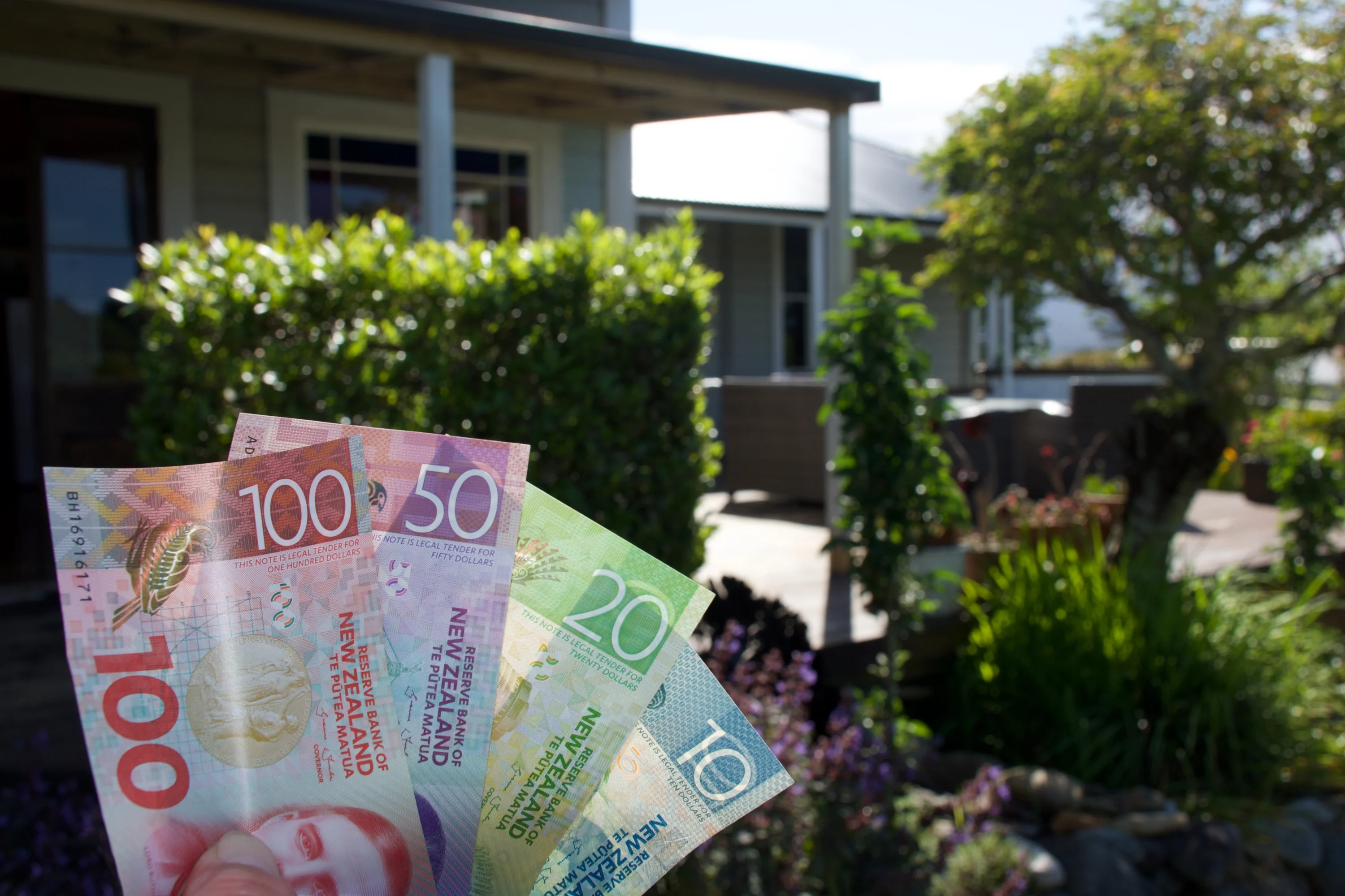 New Zealand Dollars cash (NZD) in front of a home.
