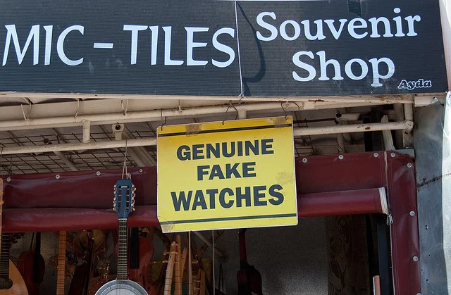 Black shop awning signs with white writing, for ceramic tiles, souvenir shop and a yellow sign with black writing  "Genuine fake watches"