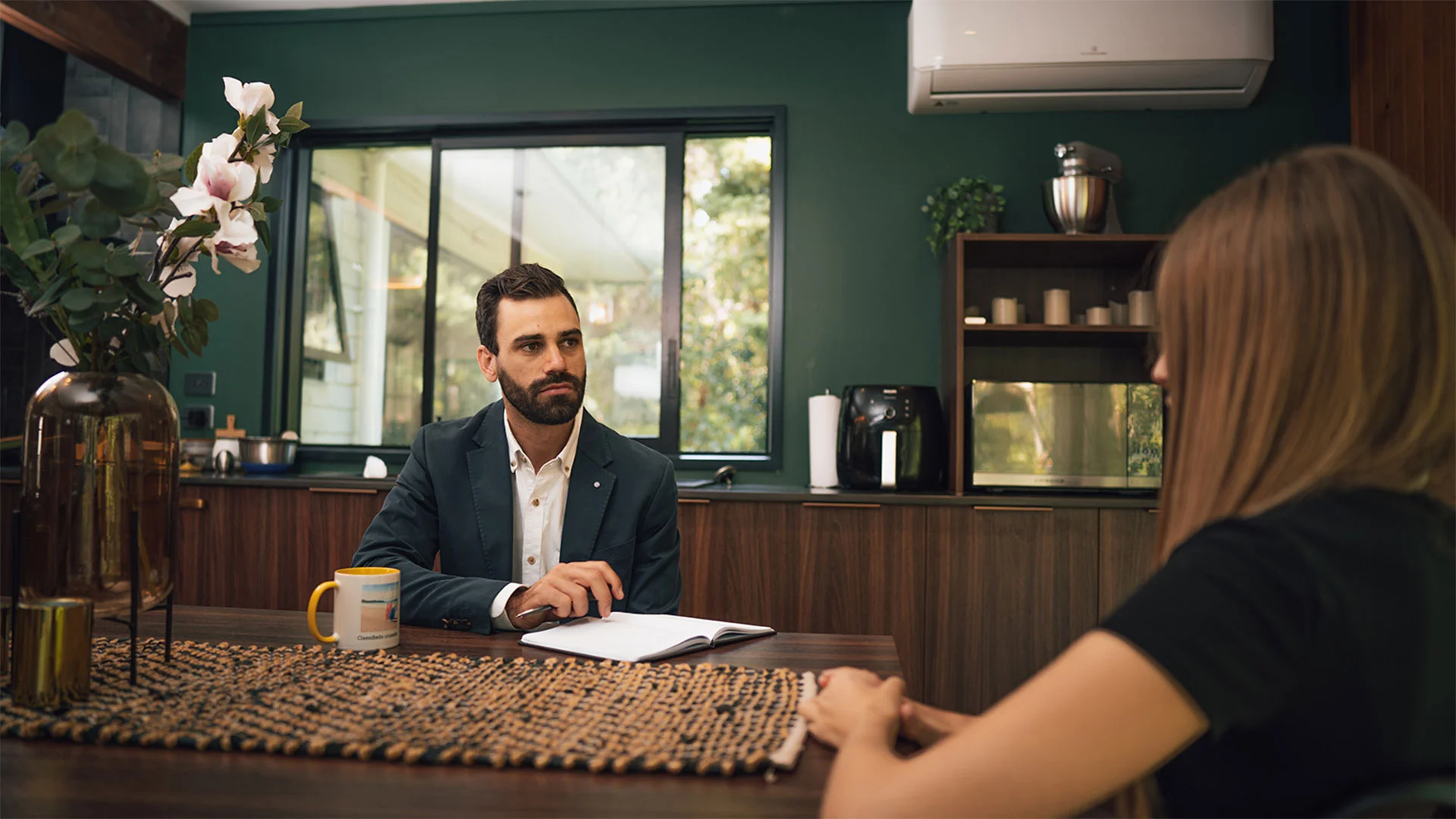 Estate agent talking to a potential buyer in a home with a notebook open on the table.