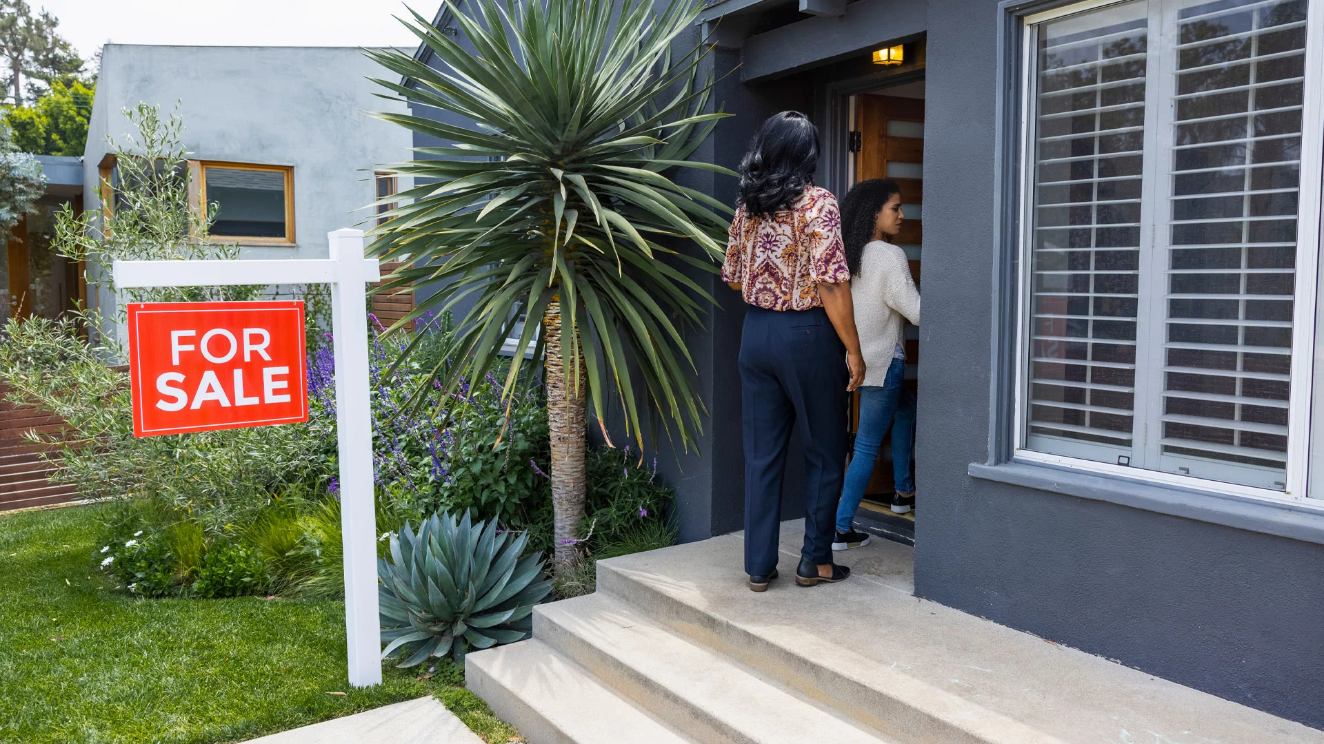 Real estate agent showing buyers into a home with a for sale sign outside.