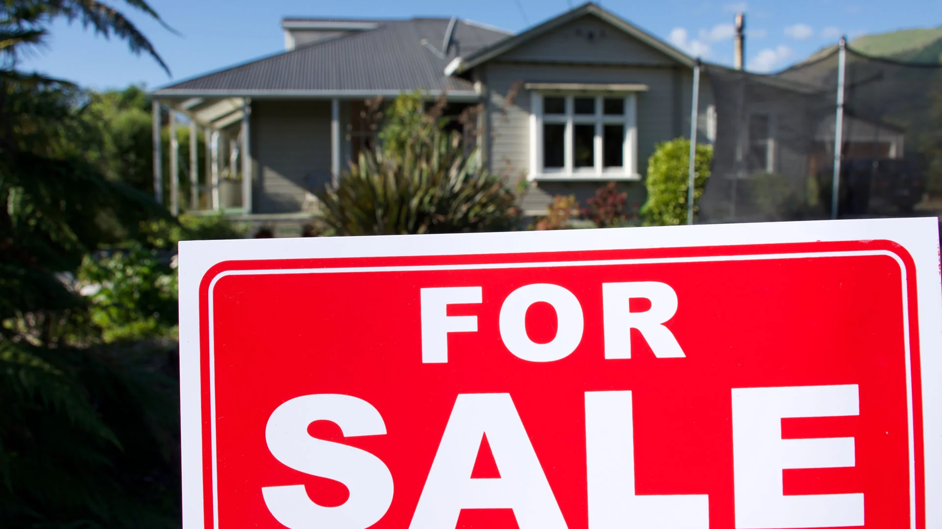 A home for sale in NZ with a "for sale" sign outside