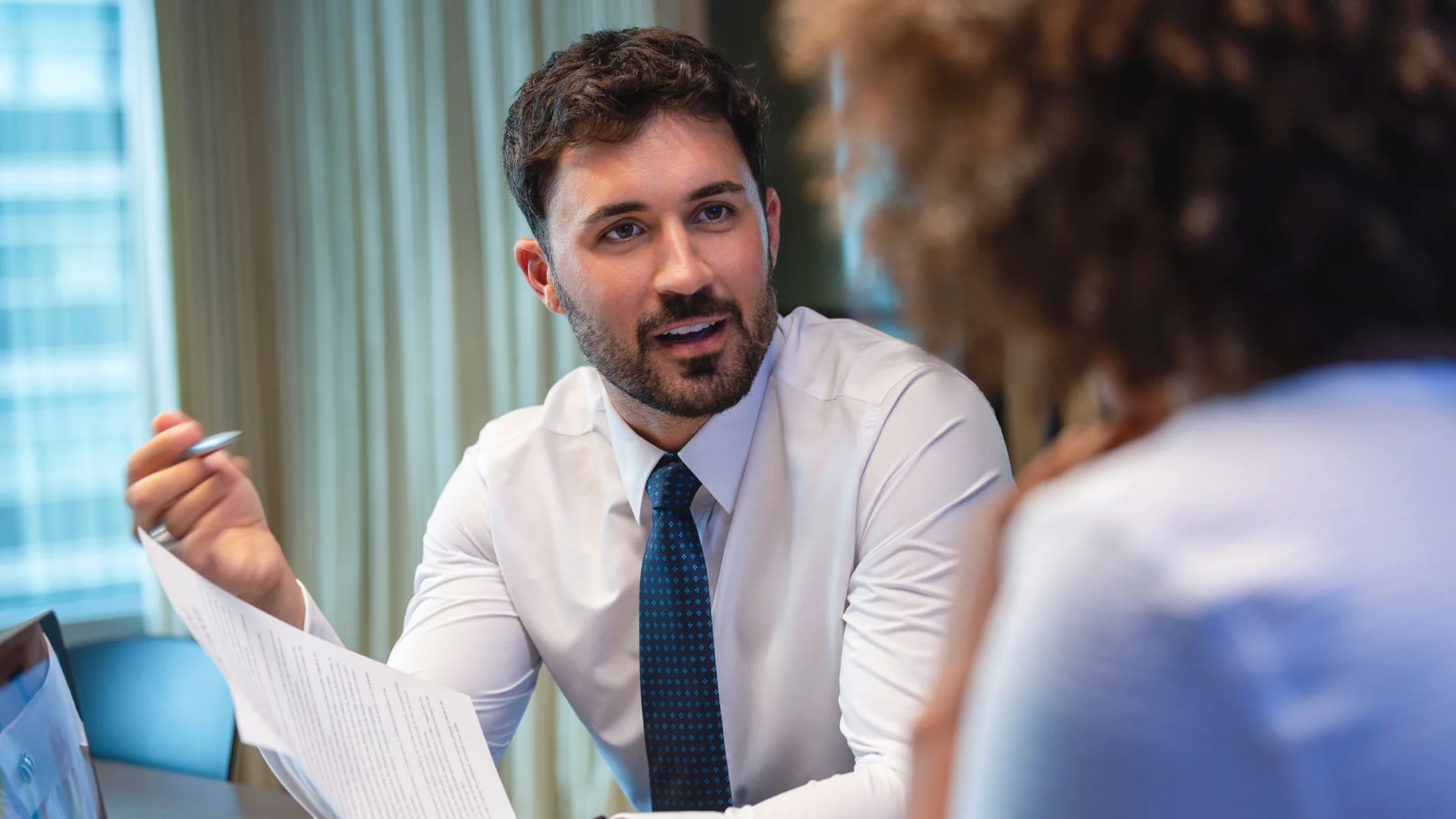 A solicitor holding a piece of paper and talking to a client in his office.