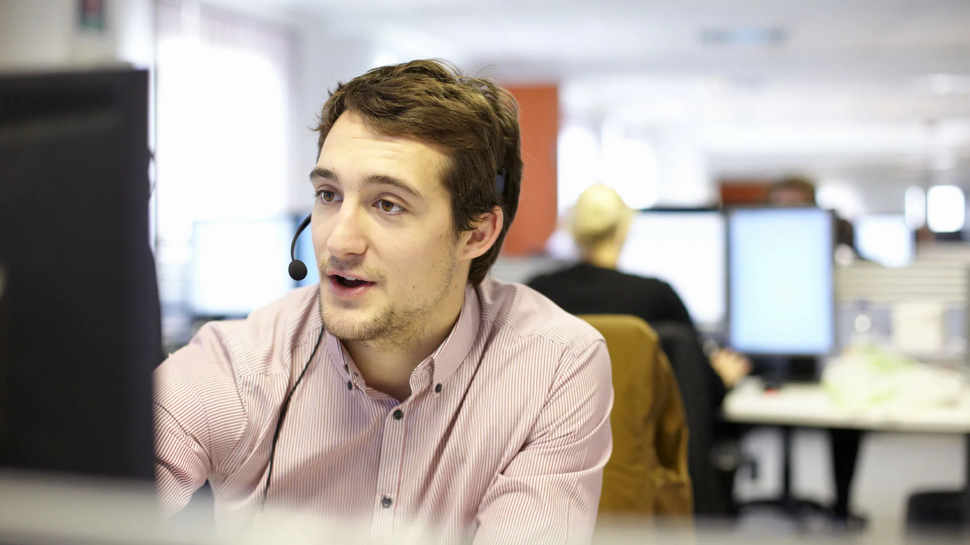 Male customer service representative speaking in to a headset in an office.