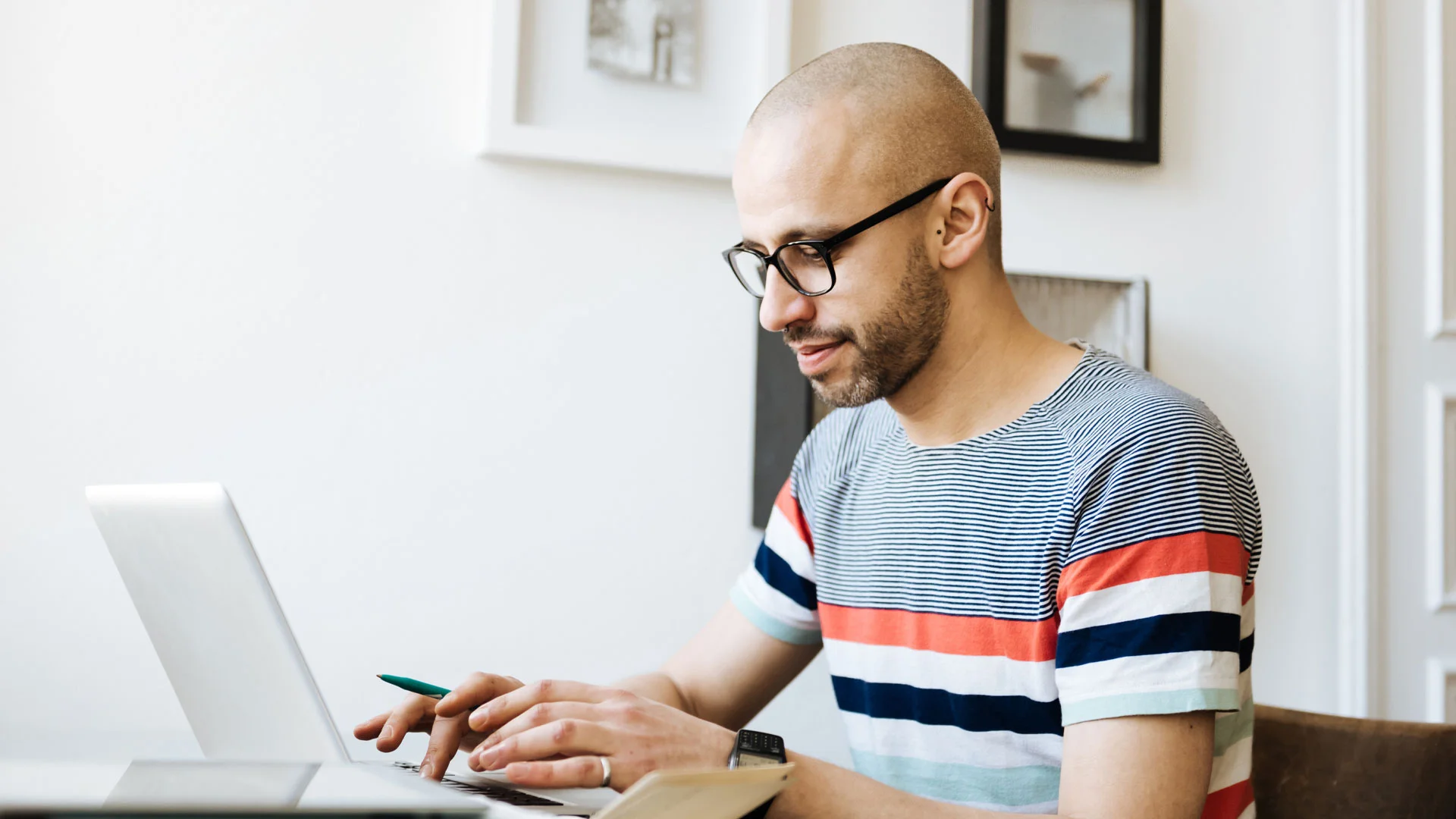Journalist writing up a story on his laptop while referring to his notepad for details.