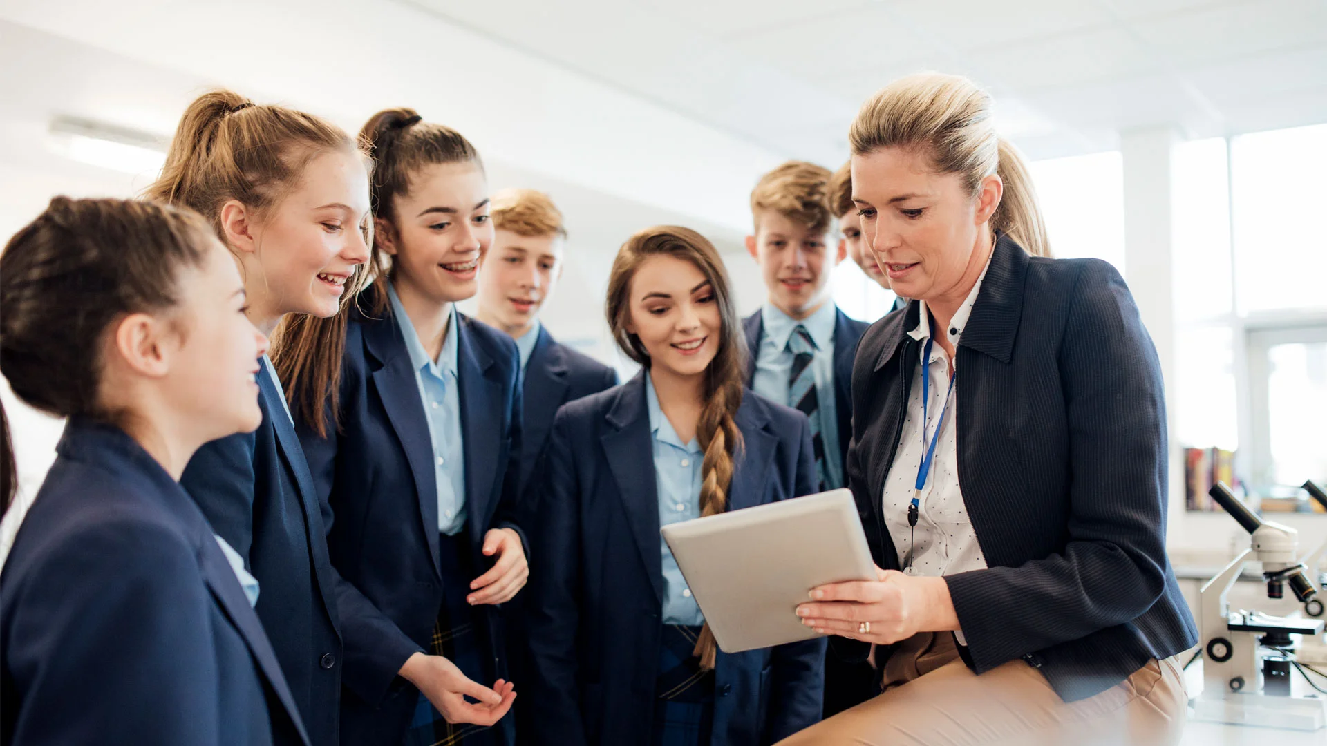 Teacher sitting with high school age students explaining something to them and showing them a tablet.