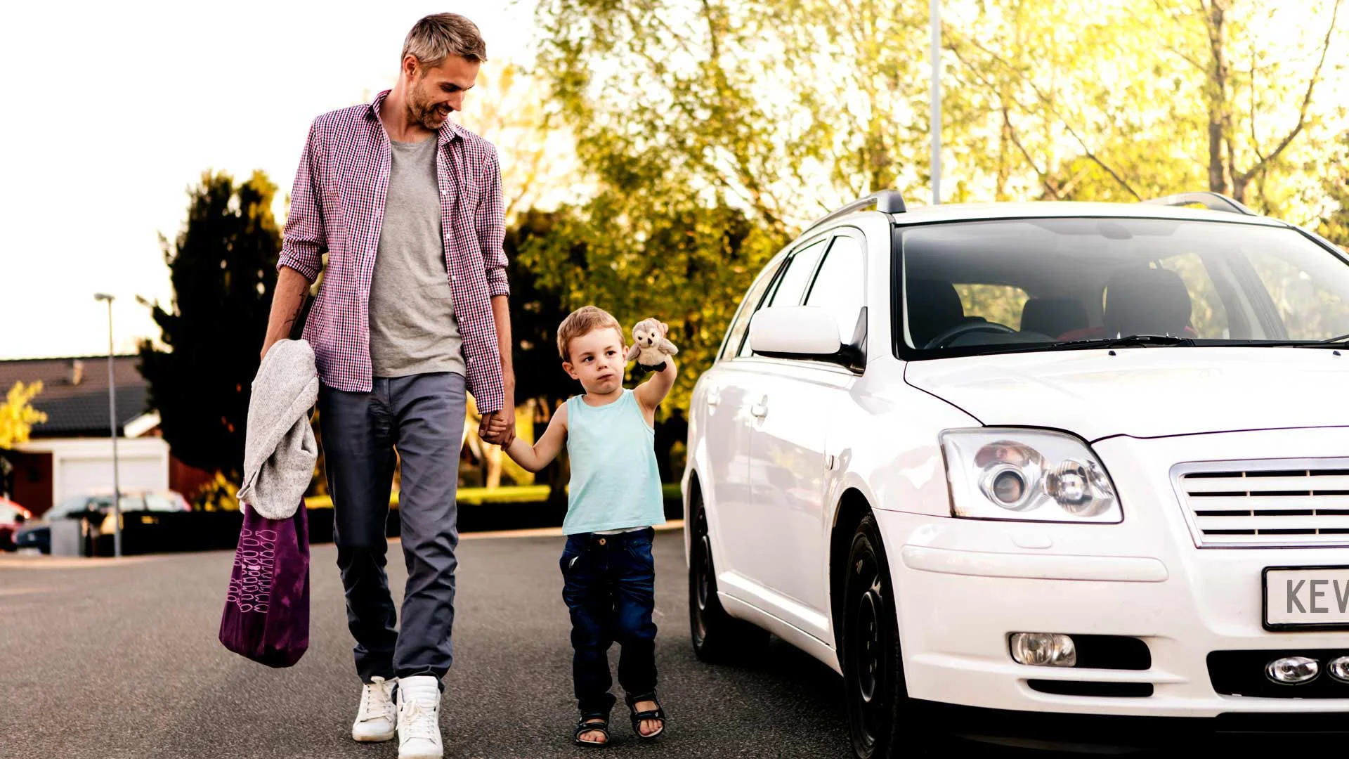 Father and son walking alongside white Toyota