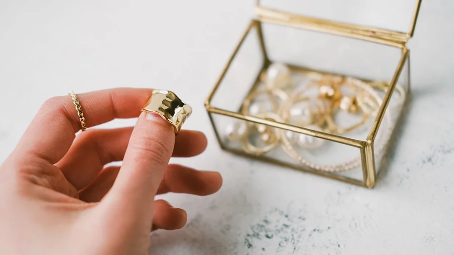 Female hand holding gold ring in front of gold jewellery box