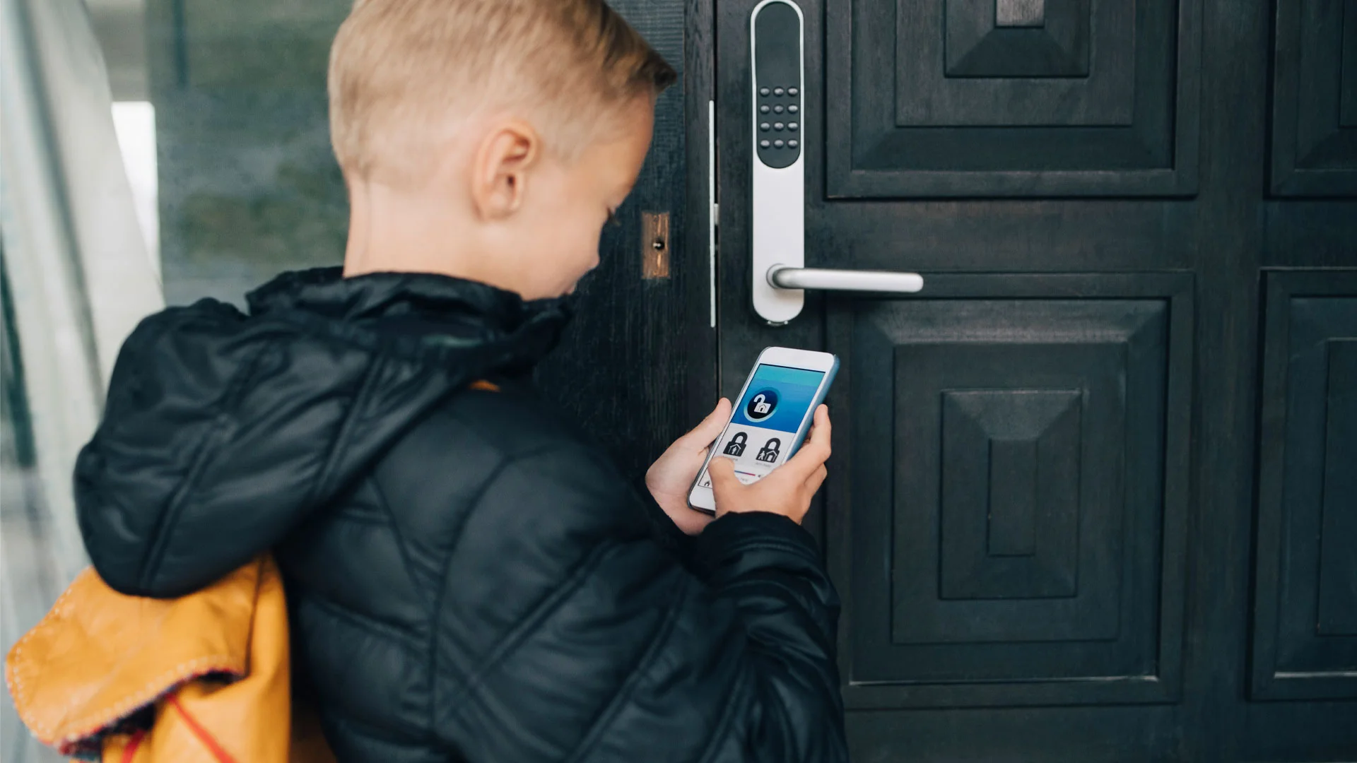 Young boy using his phone to open the smart lock on the front door of his home.
