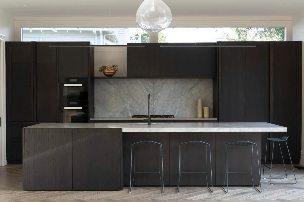 Front on view of kitchen with dark cupboards and high stools sitting at the bench