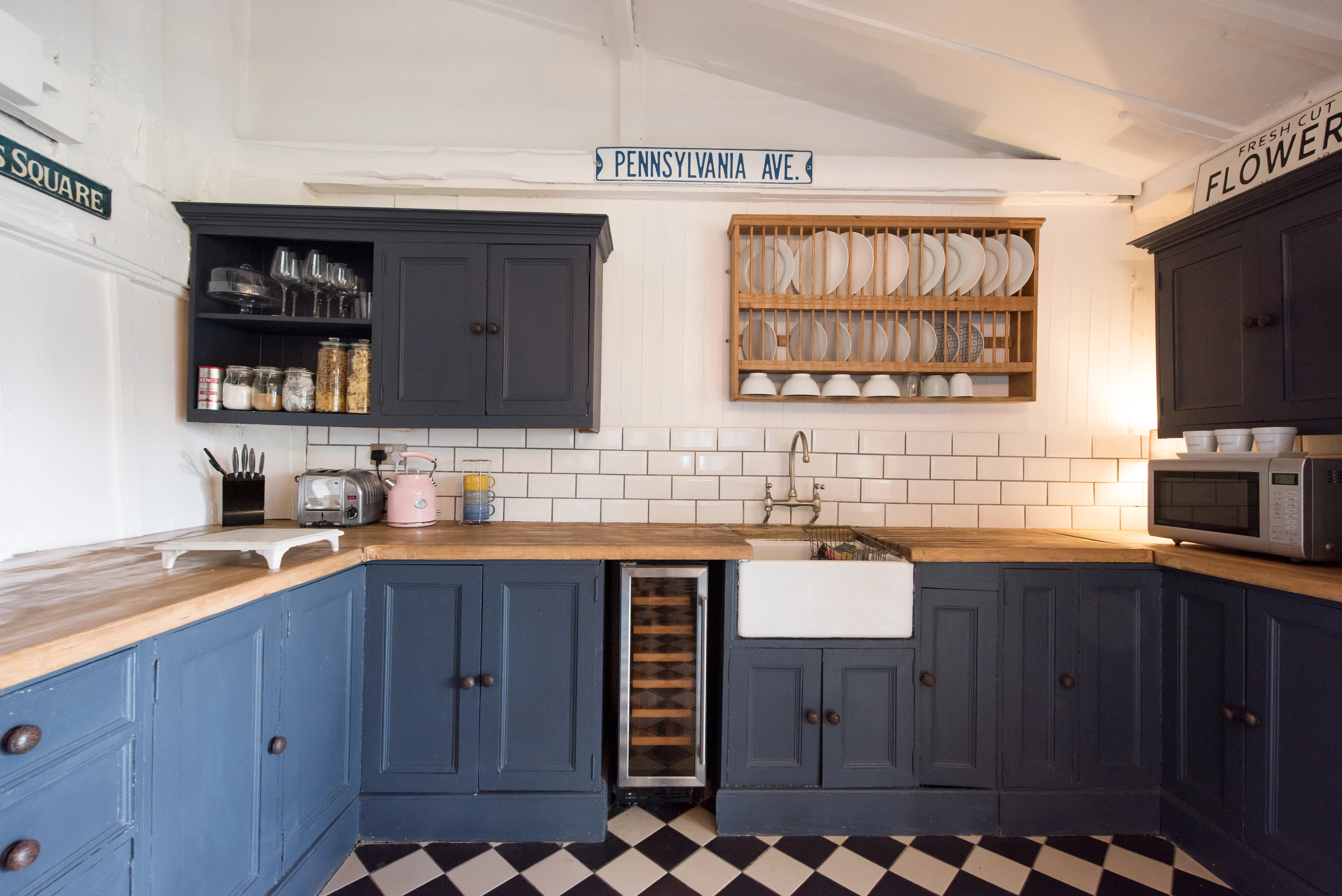 Dark blue kitchen cabinets with a wooden kitchen top. A butler sink with brass taps and statement black and white flooring.