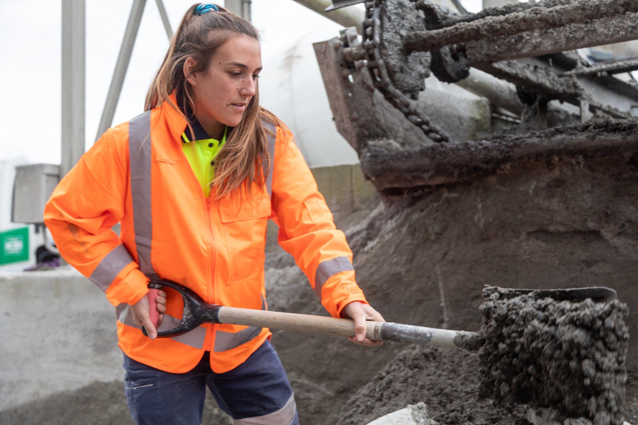 Young female labourer shoveling concrete outside