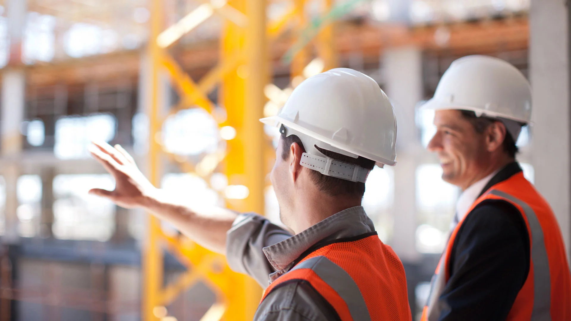 Two men on a construction site in high vis jackets and hard hats planning the next phase of work.