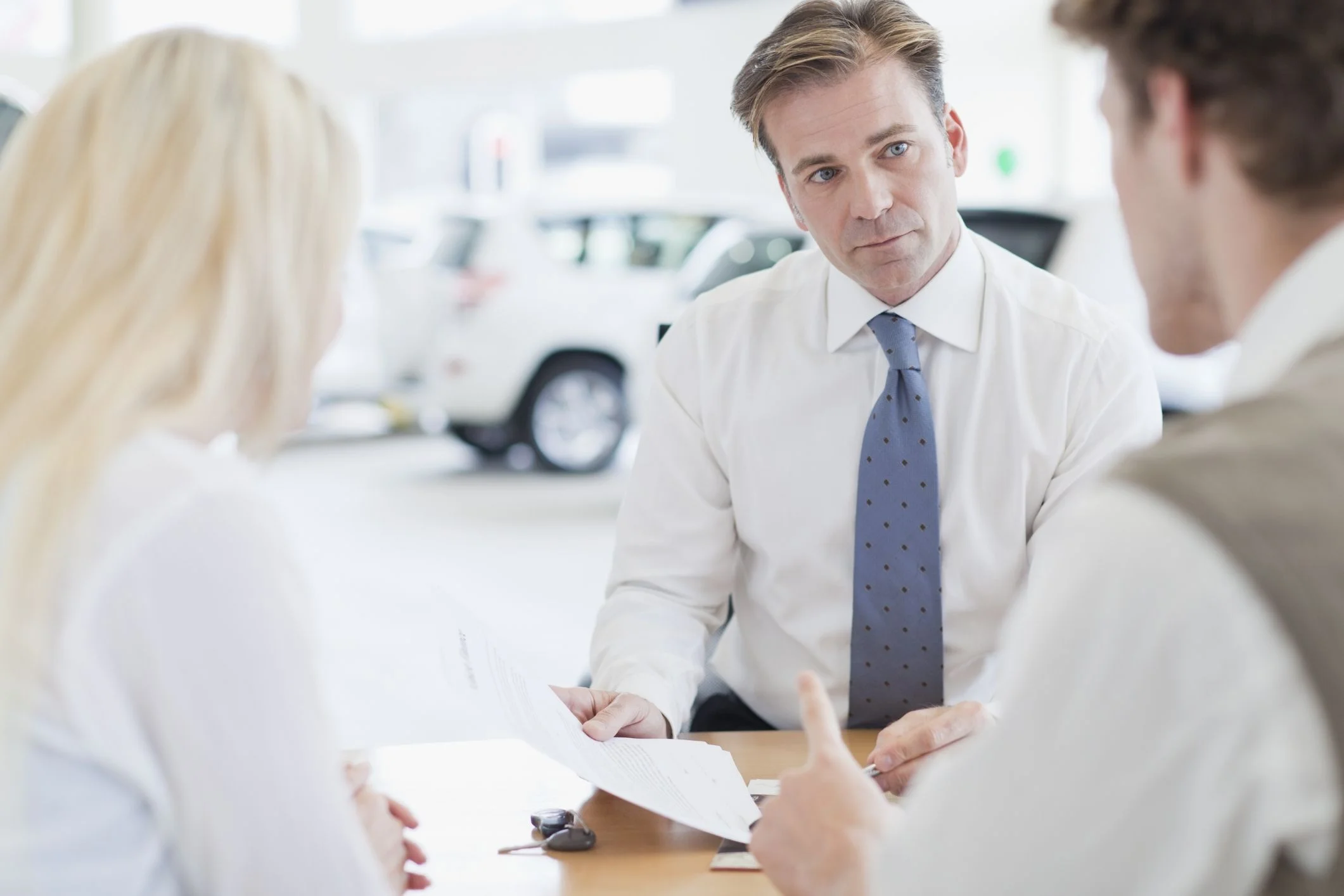 Car sales man talking through paper work with couple.