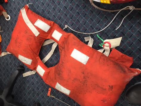 An old bright orange lifejacket, the type that goes over your head, with reflective strips, lying on dark coloured carpet
