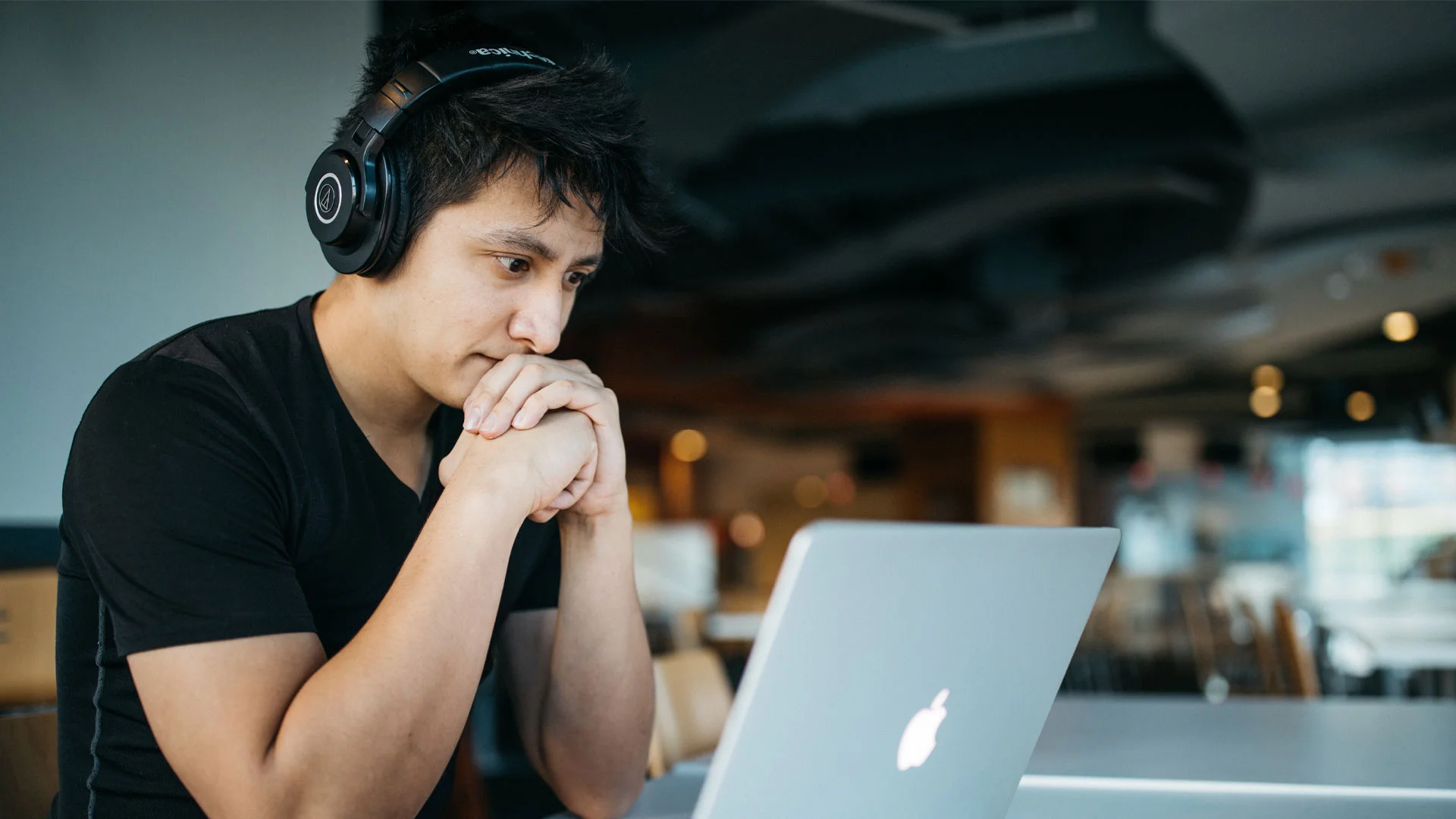 Young man staring at his laptop screen as he uses ChatGPT to help him write his CV.