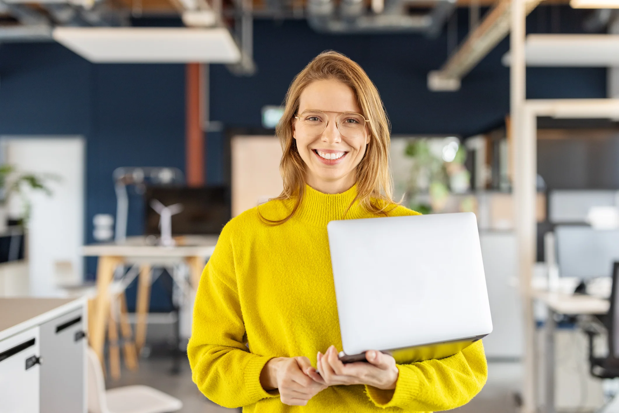 Lady in yellow jumper holding laptop.