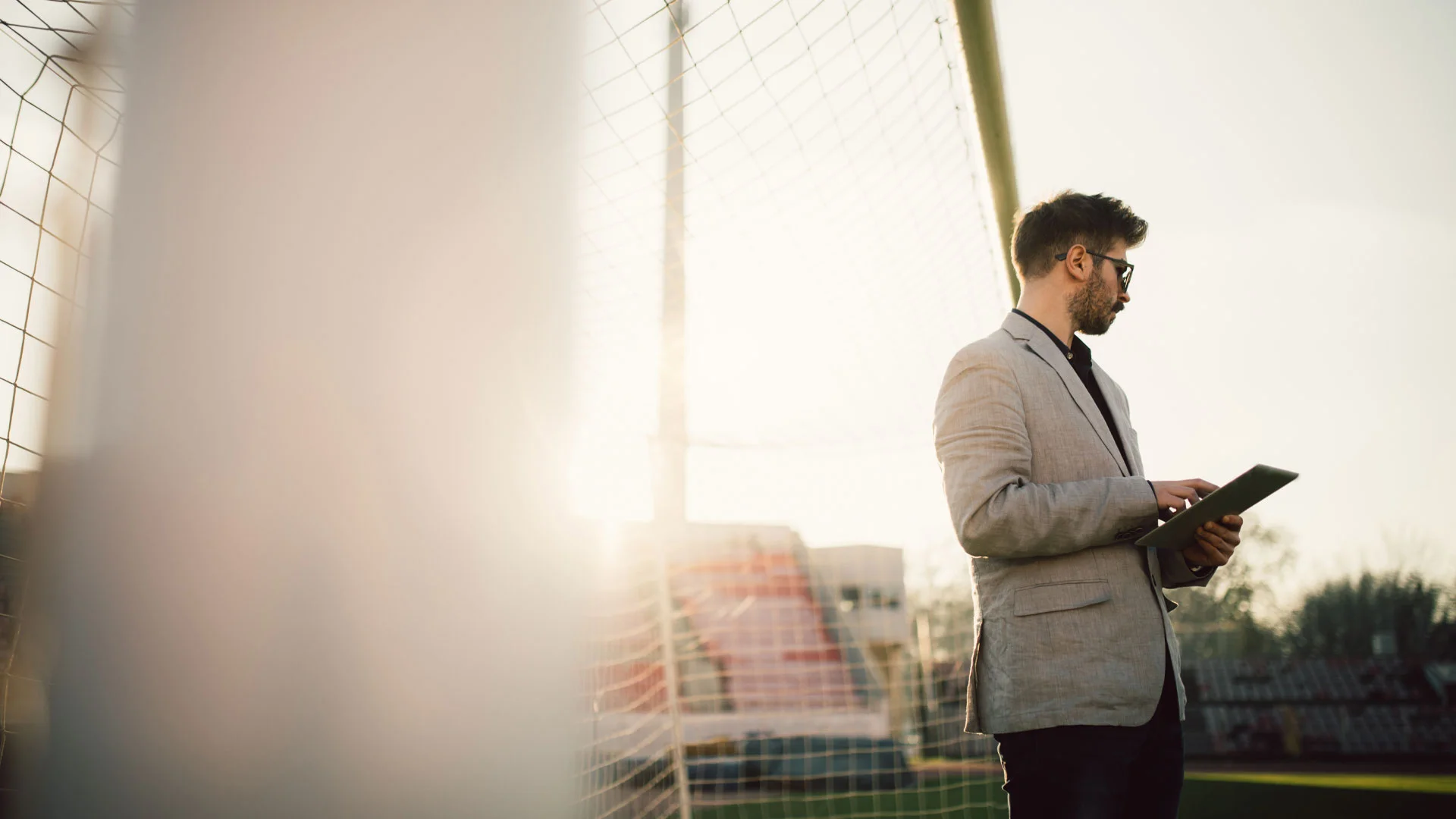 Sports journalist standing with a digital tablet under a football goal.
