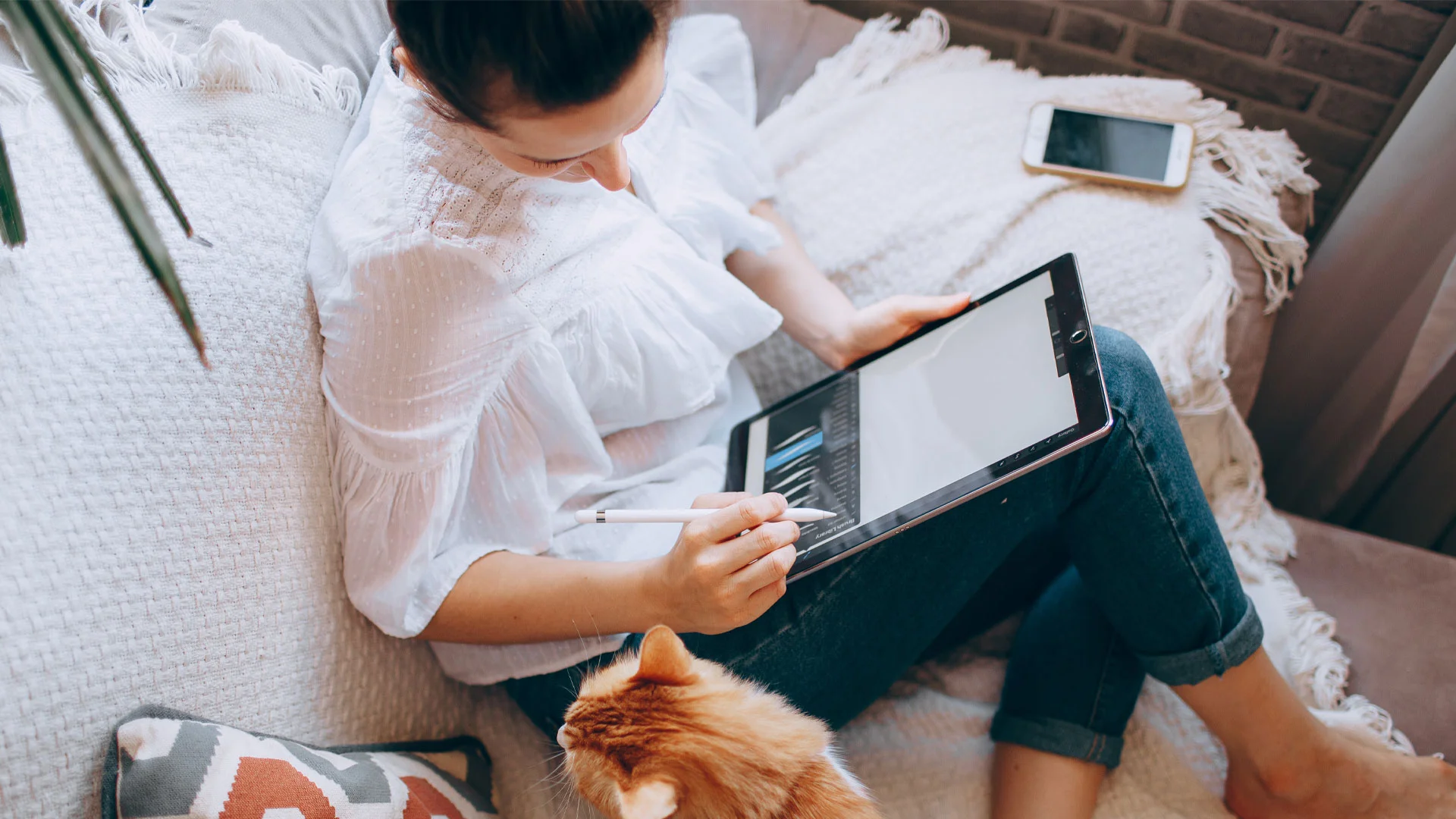 Woman working on a tablet on her couch with her cat.