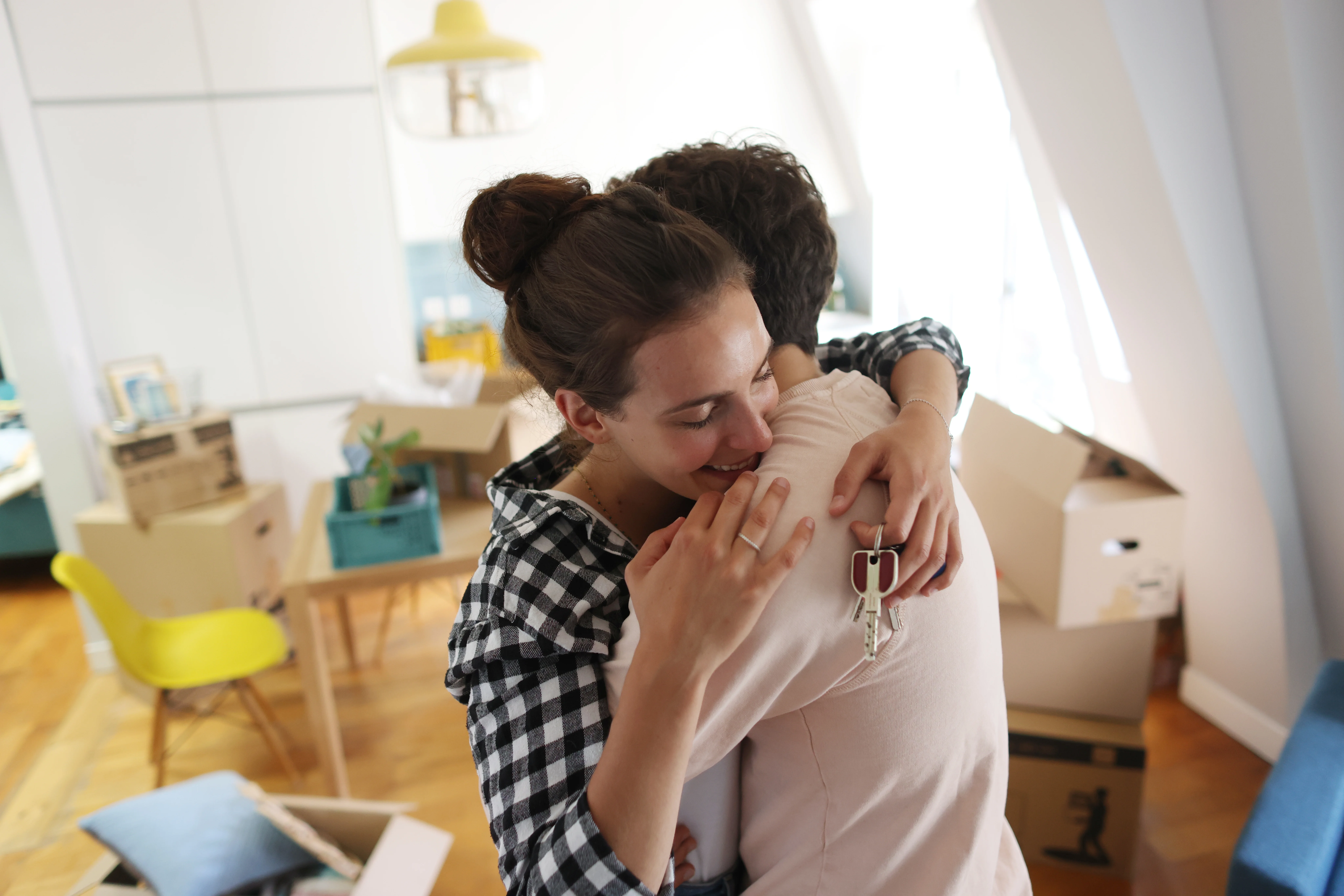 A man and woman embrace in a hug as she holds a house key symbolising that they have just bought a new house.