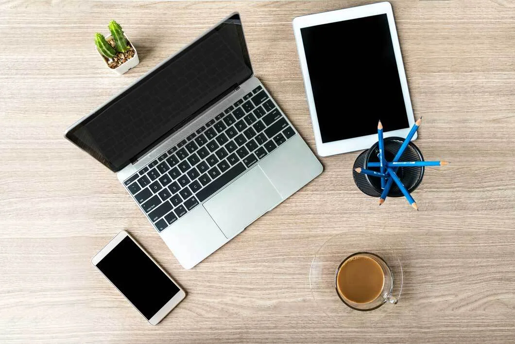 Aerial view a refurbished mobile phone, laptop and tablet on a wooden table next to a cup of coffee.