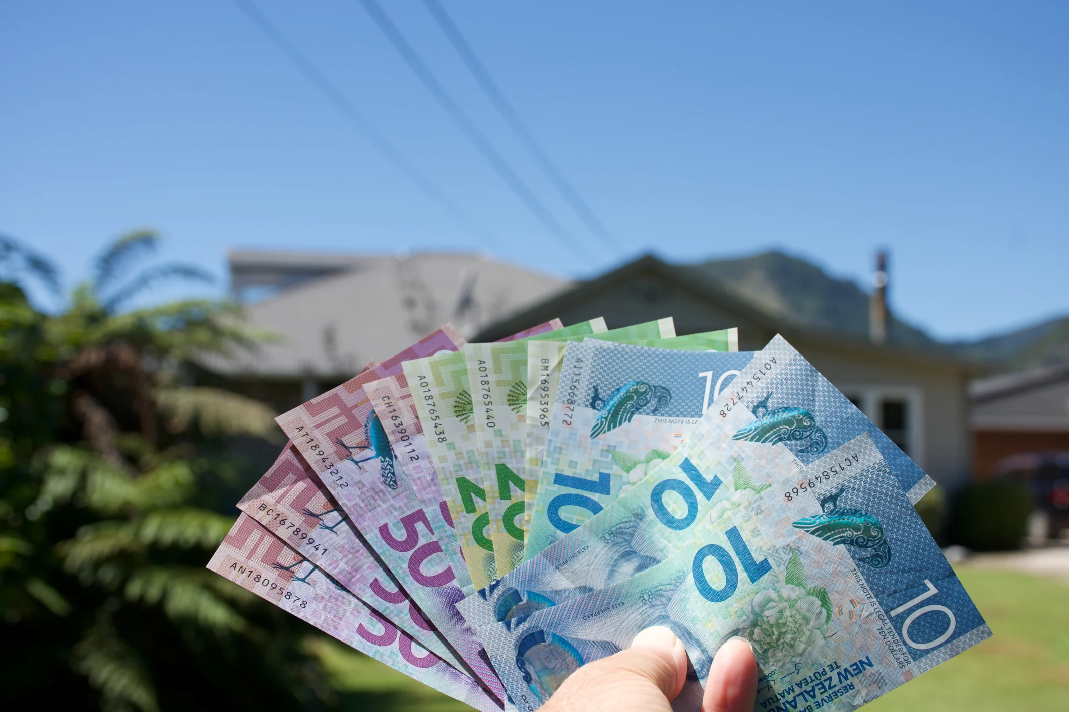 Hand holding cash in front of property. 