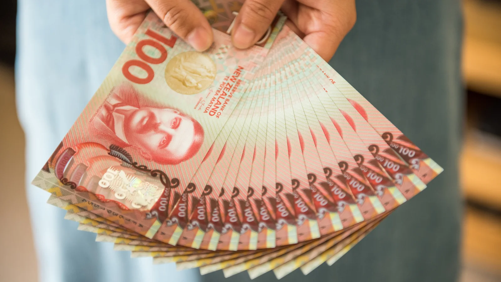 NZD $100 notes in hand.