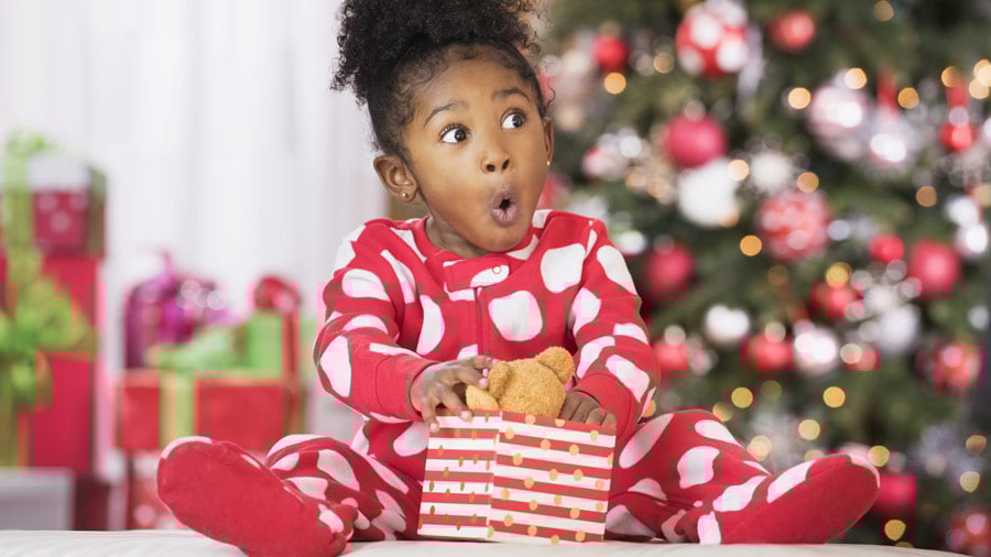 A very excited kid opens a toy in front of a Christmas tree