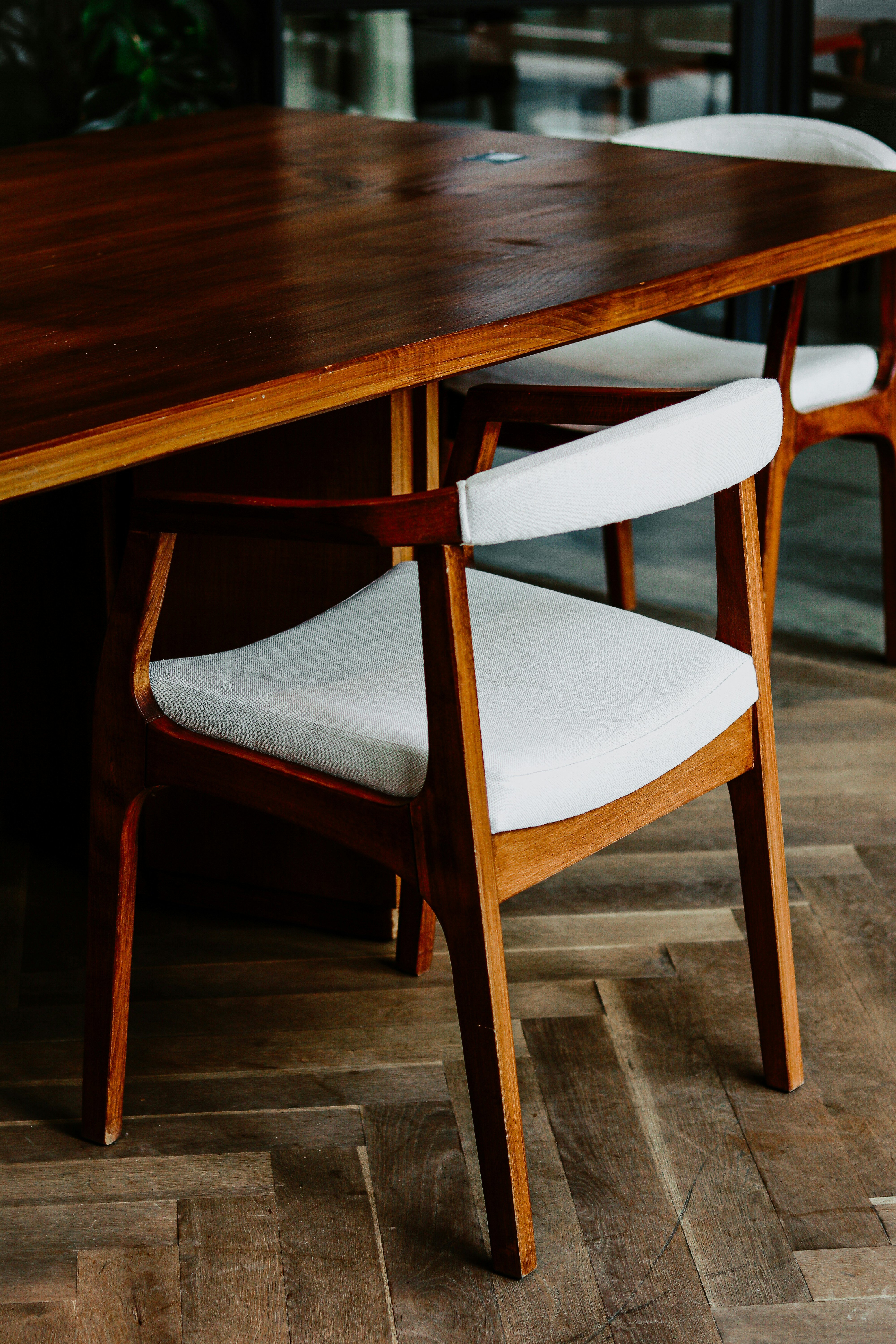 A wooden dining chair with a curved backrest and light grey upholstered seat, pulled up to a dark timber table on a herringbone floor.