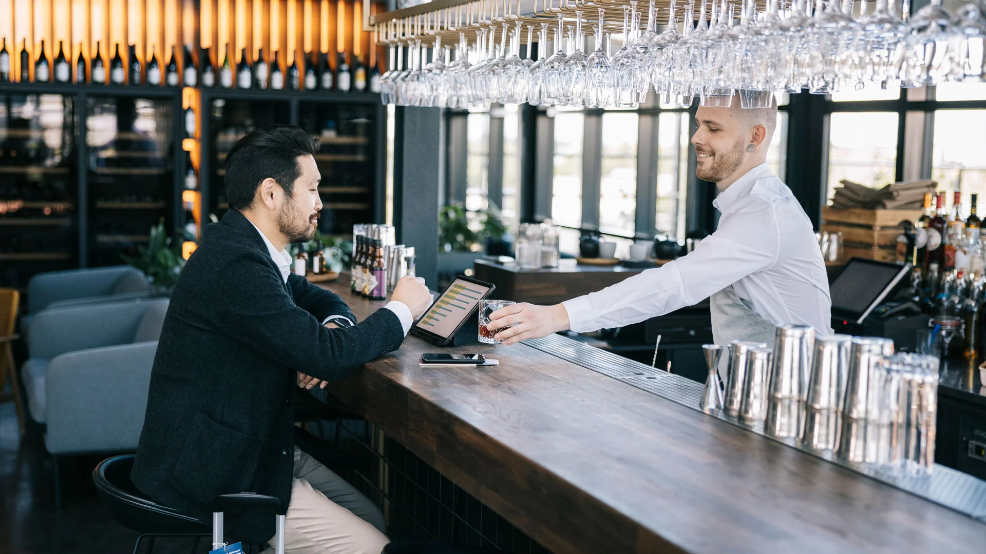 Barman working behind a bar in an airport serving drinks to a patron.