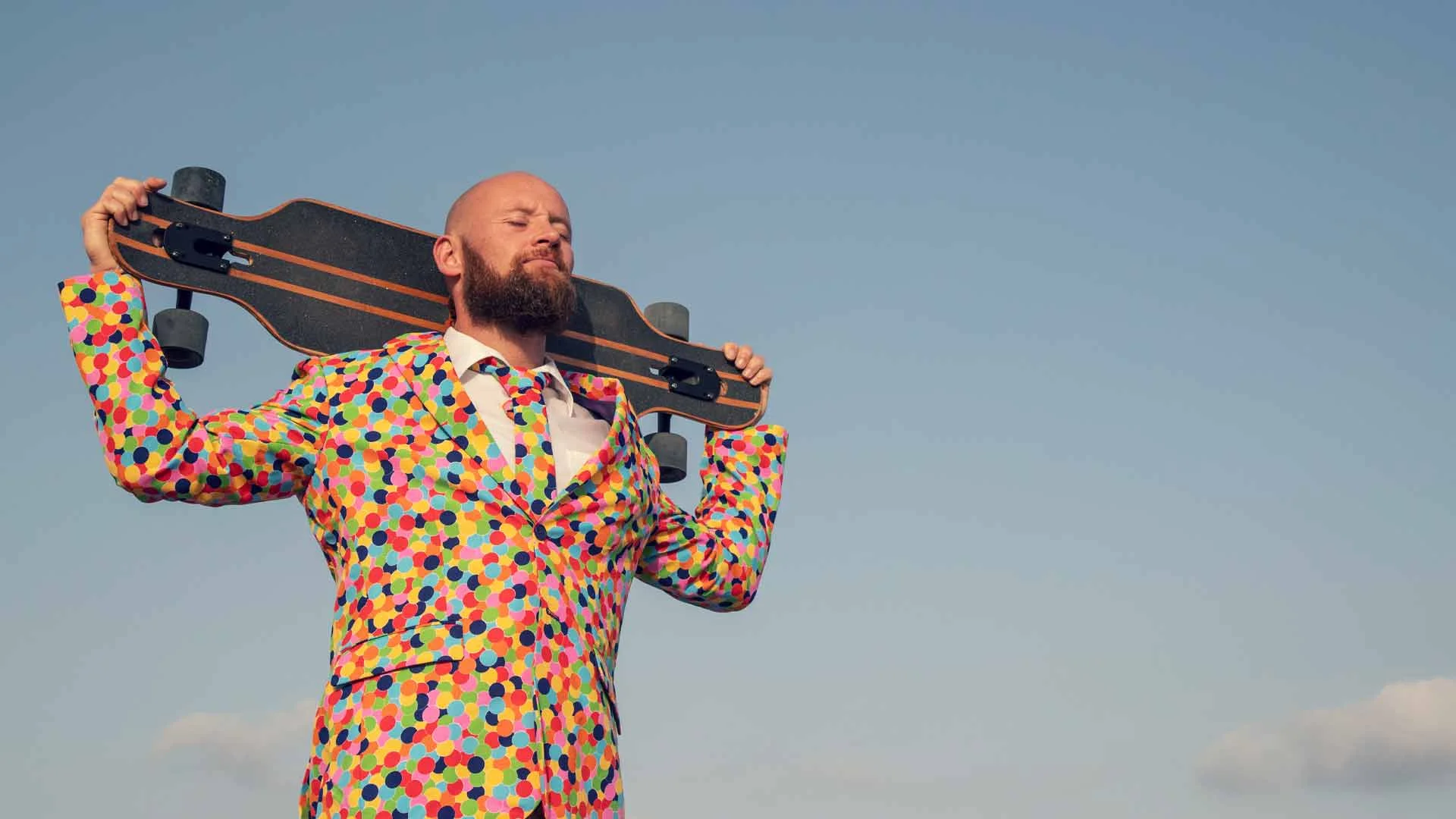 Man in vibrant suit holding a skateboard.