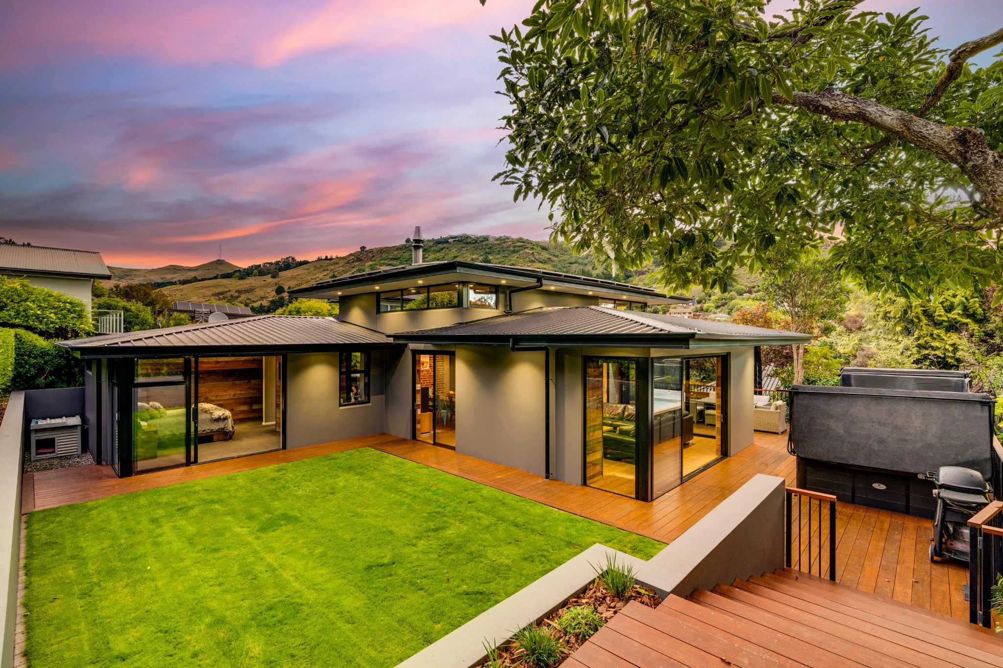 Modern wooden and black house sits below a pink and purple sky.