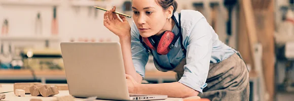 A women looking at her laptop and holding a pencil. 