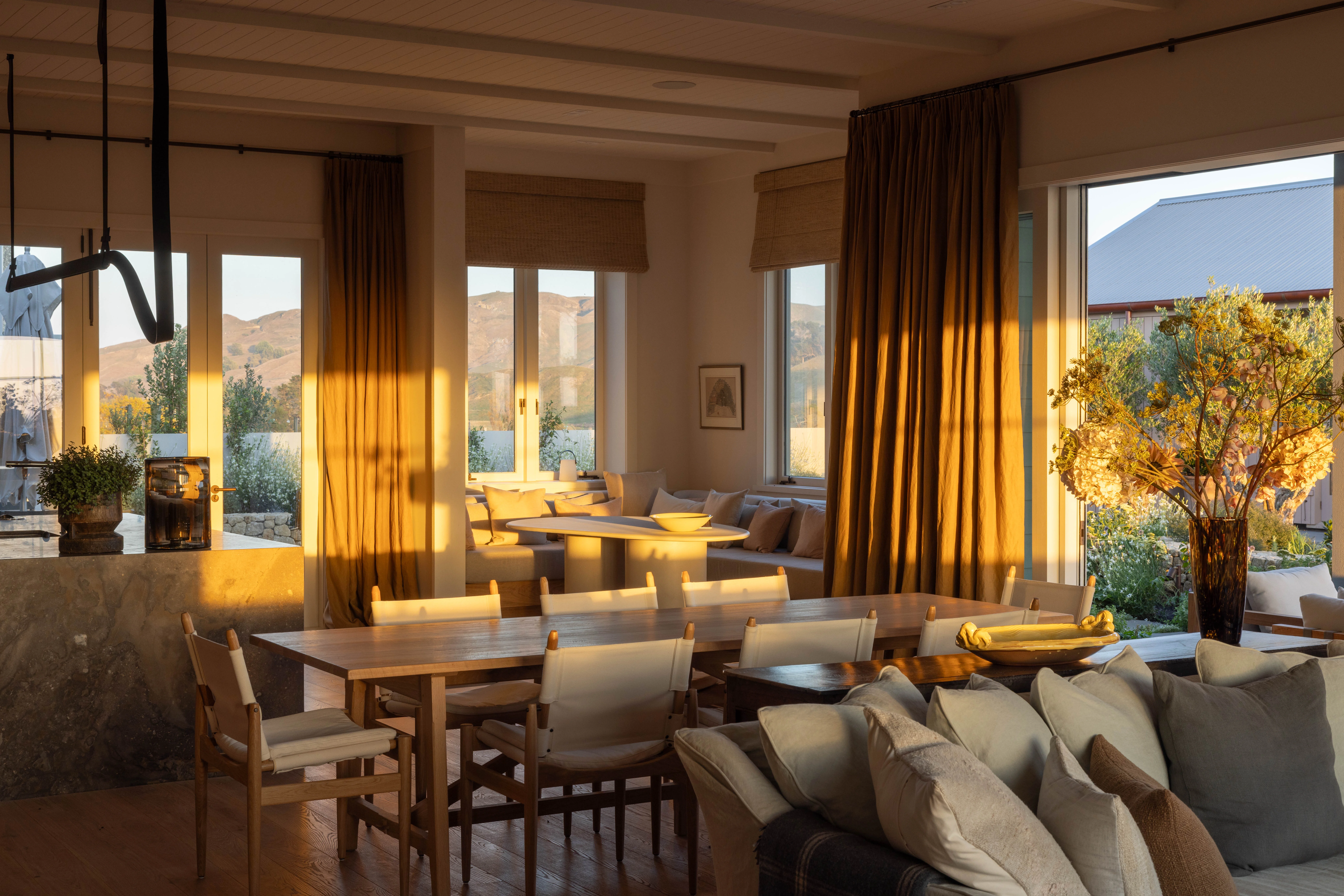 An antique French oak Orangery dining table, custom-made to size by John Stephens & Company, and teamed with Stellar Works Journey dining chairs, gets a view north to the hills of the equestrian farm. Brigit Christie had the drapes made from James Dunlop Satori Stonewash linen in Ochre to reflect “the colours all around”.