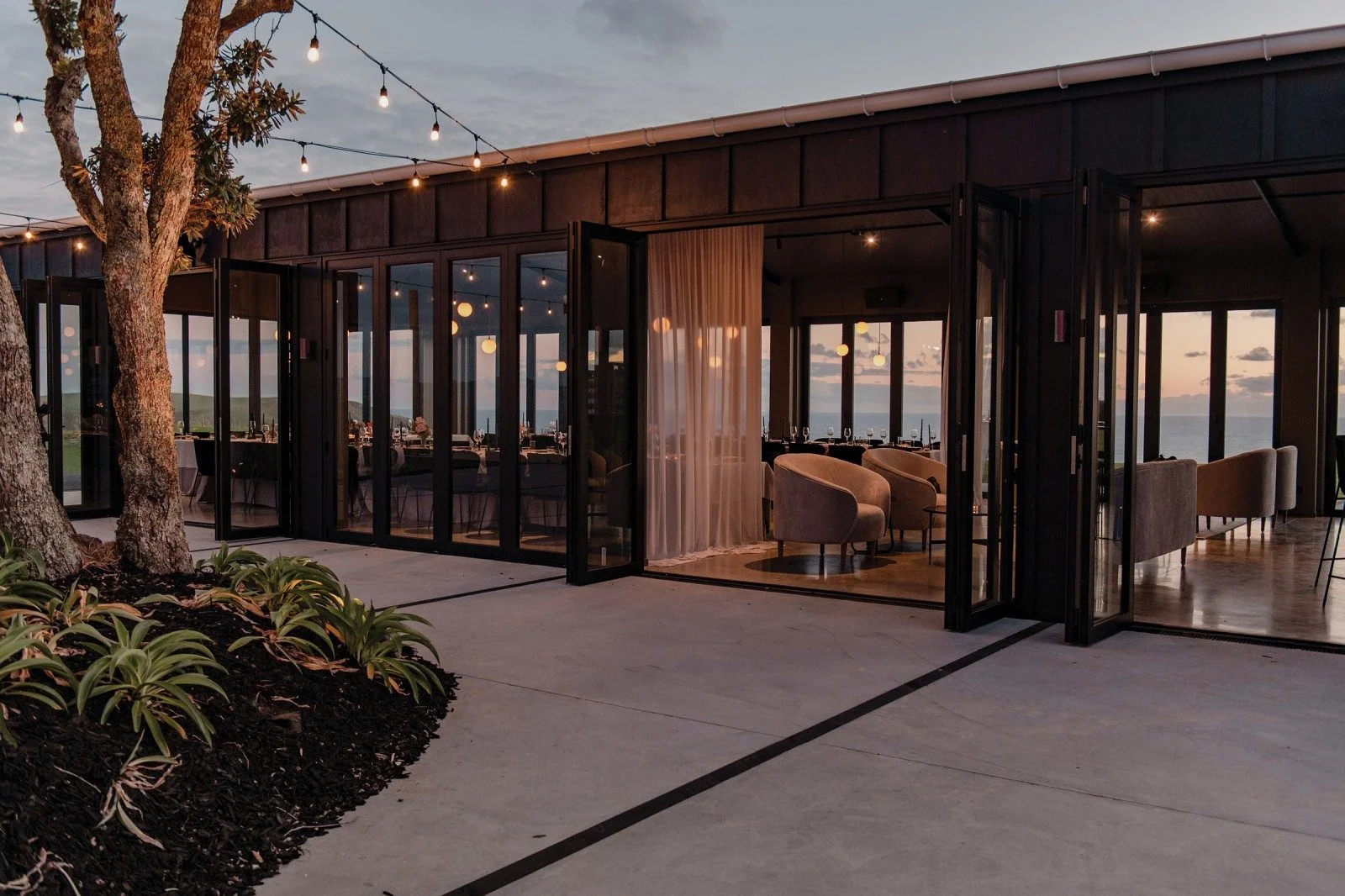 Contemporary clifftop venue at Parihoa Estate, one of New Zealand’s most expensive houses, featuring modern architecture, open dining spaces, and ocean views at sunset.