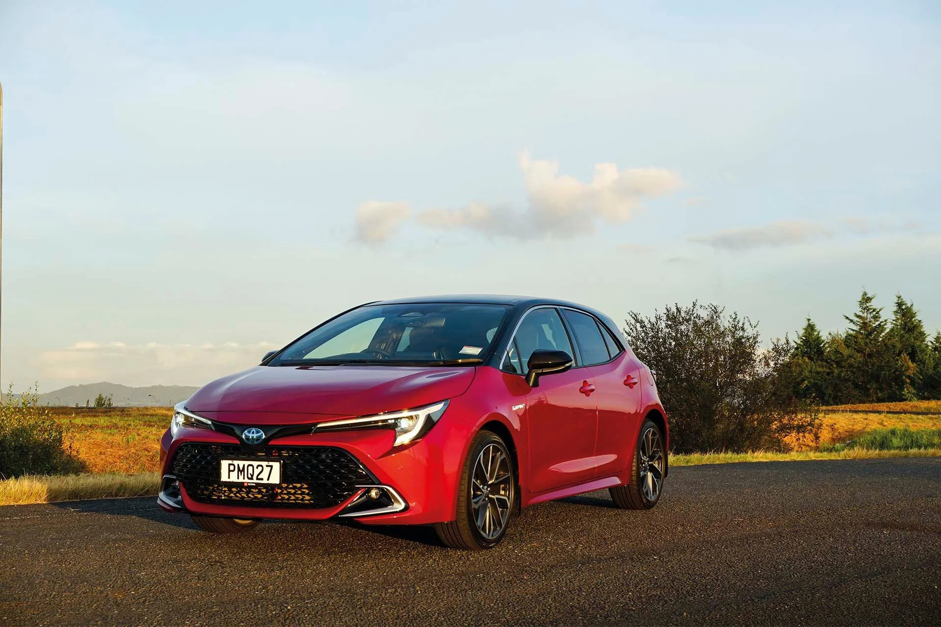 Red Hybrid Toyota Corolla front end stationary on road.