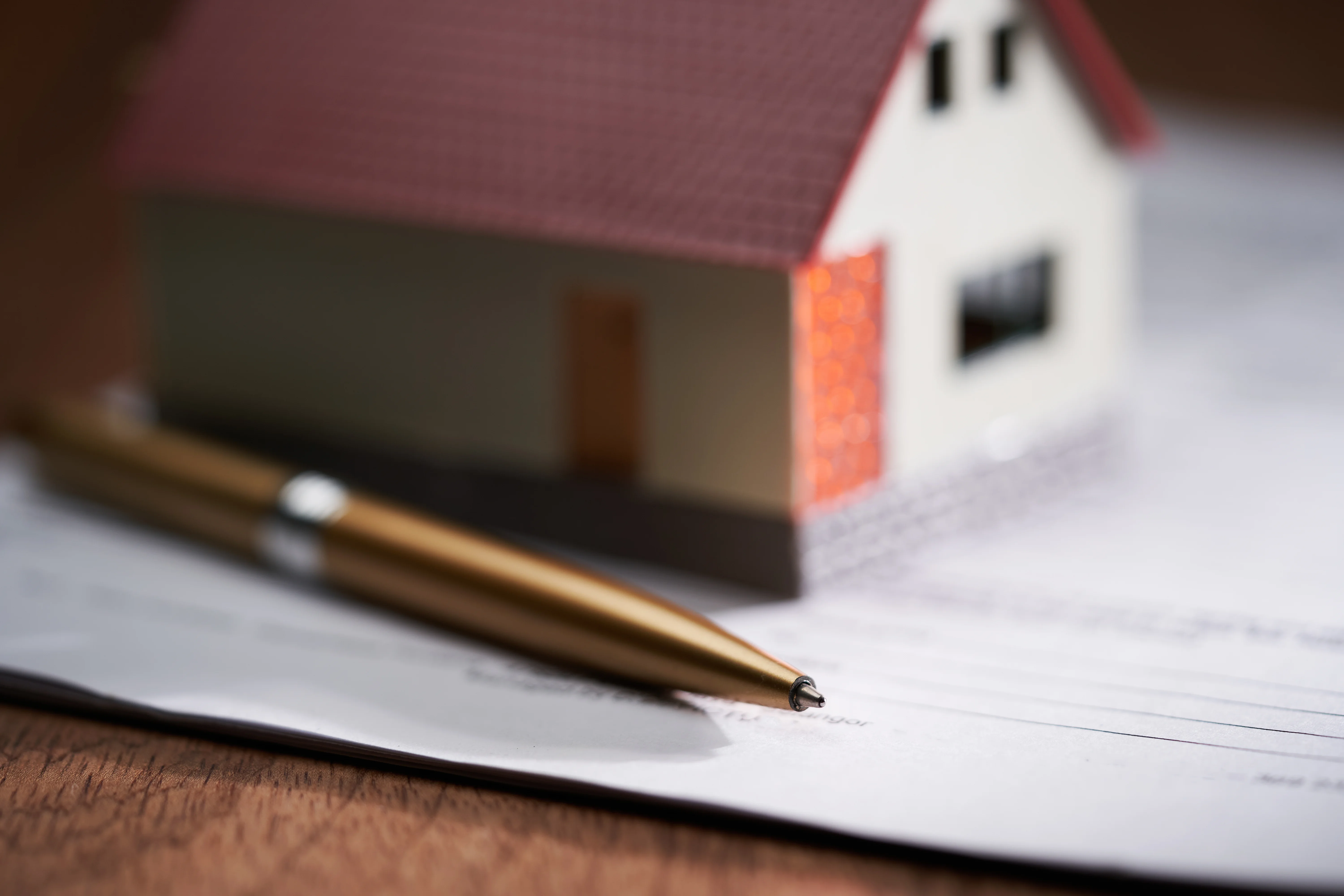 Small toy house sits on top of papers and next to a pen