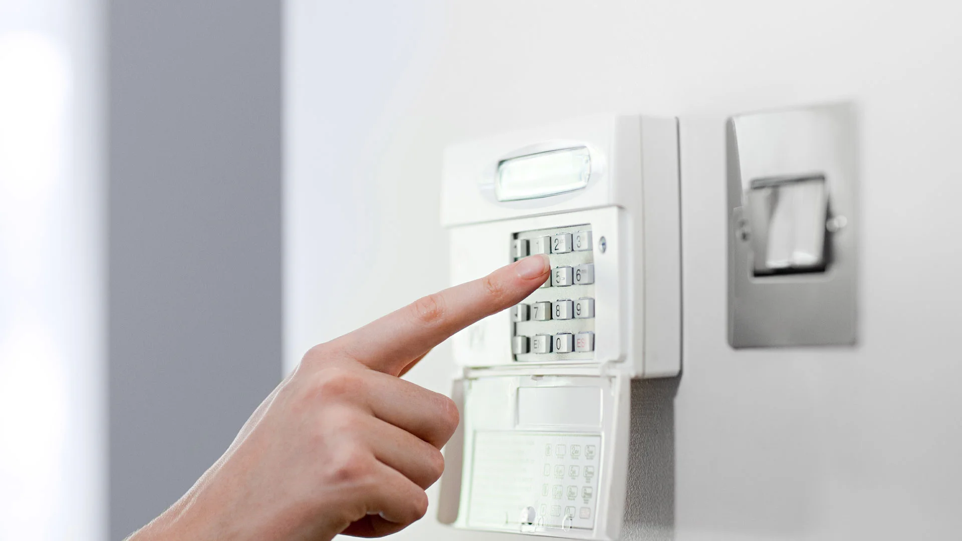 Close up of a person's hand typing in to an alarm box on the wall of a home in New Zealand.