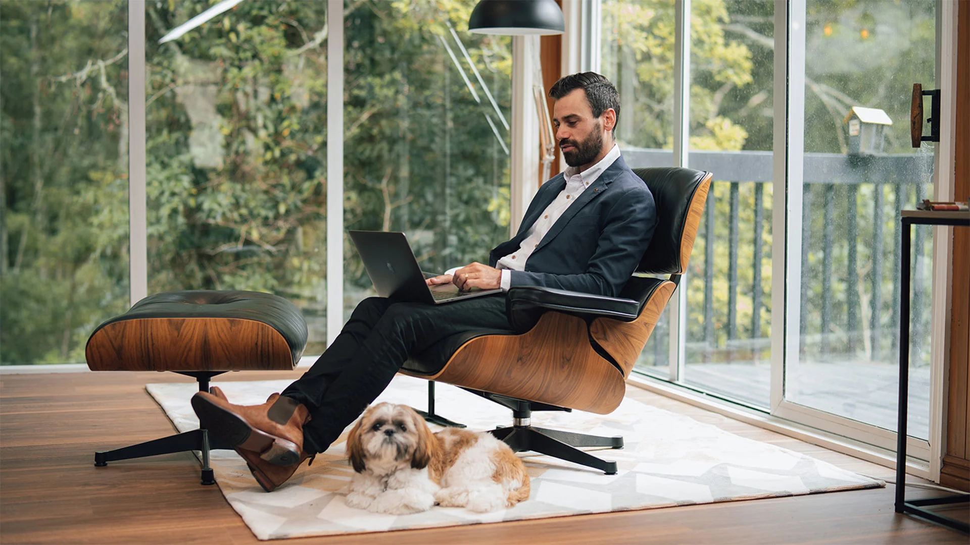 Man in a suit at home sitting in a chair reading about interest rates on his laptop.