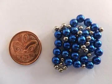 A NZ 10cent coin, to the right of it a pile of magentic blue and silver very small magnetic balls