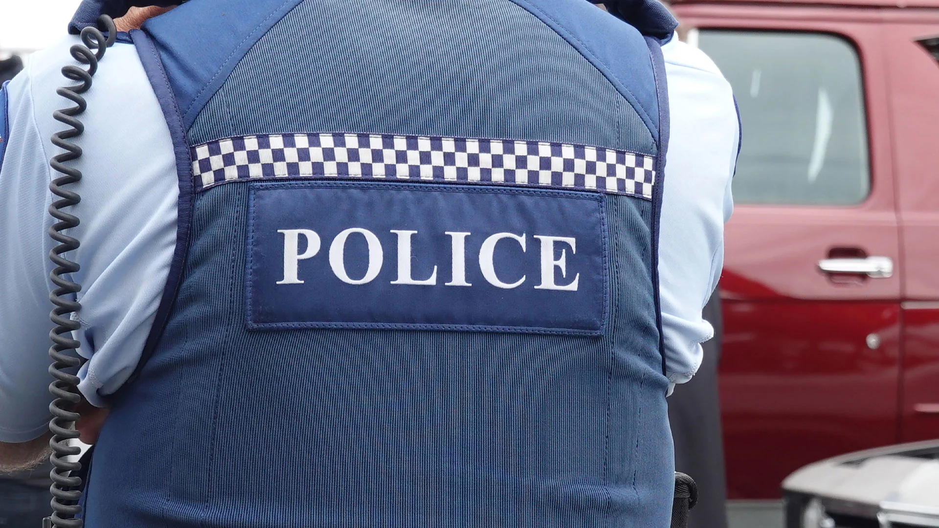 NZ police officer standing with their back to the camera, wearing a jacket that says NZ Police.