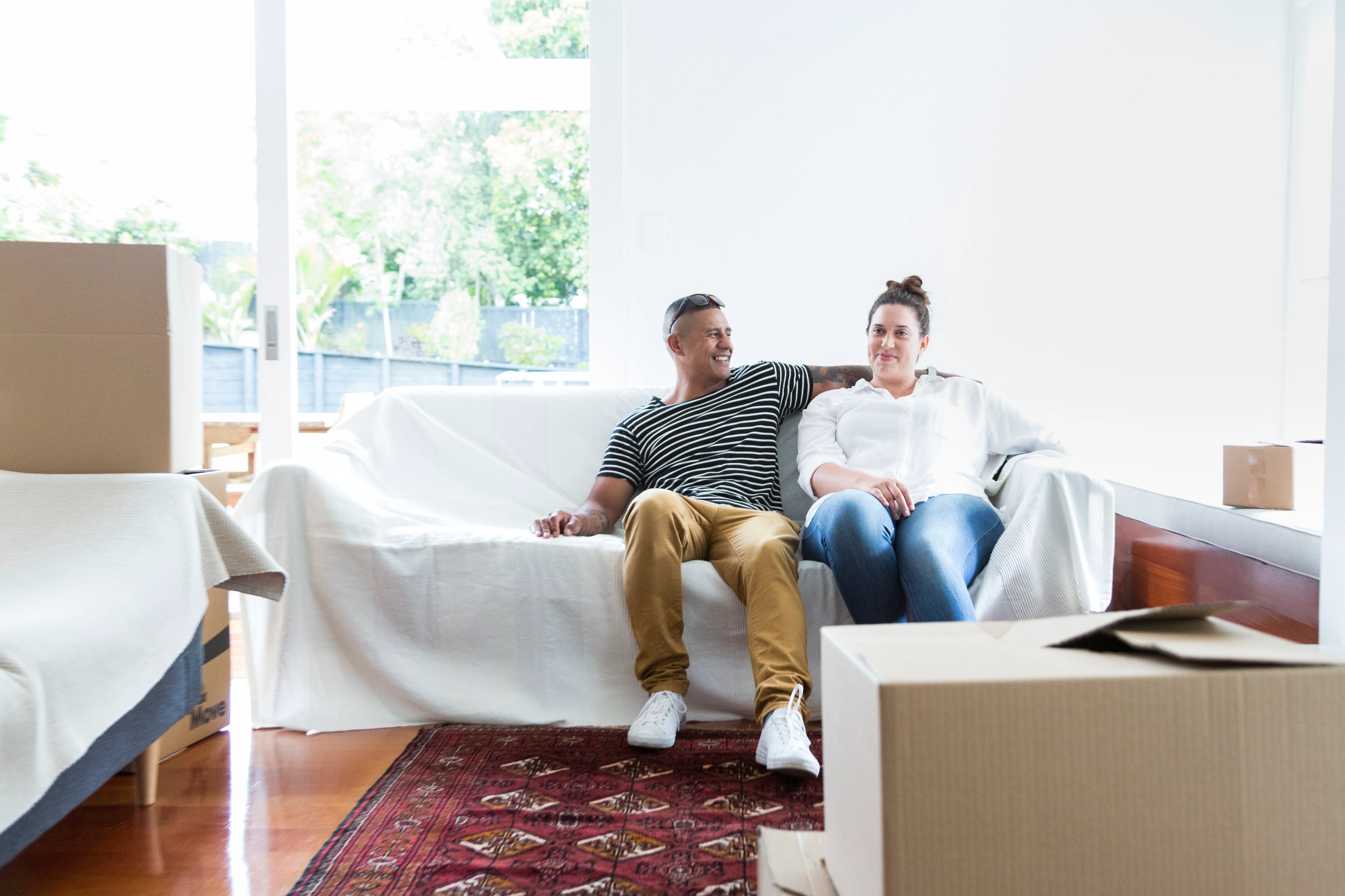 A couple relaxing on a couch in their new home surrounded by moving boxes.