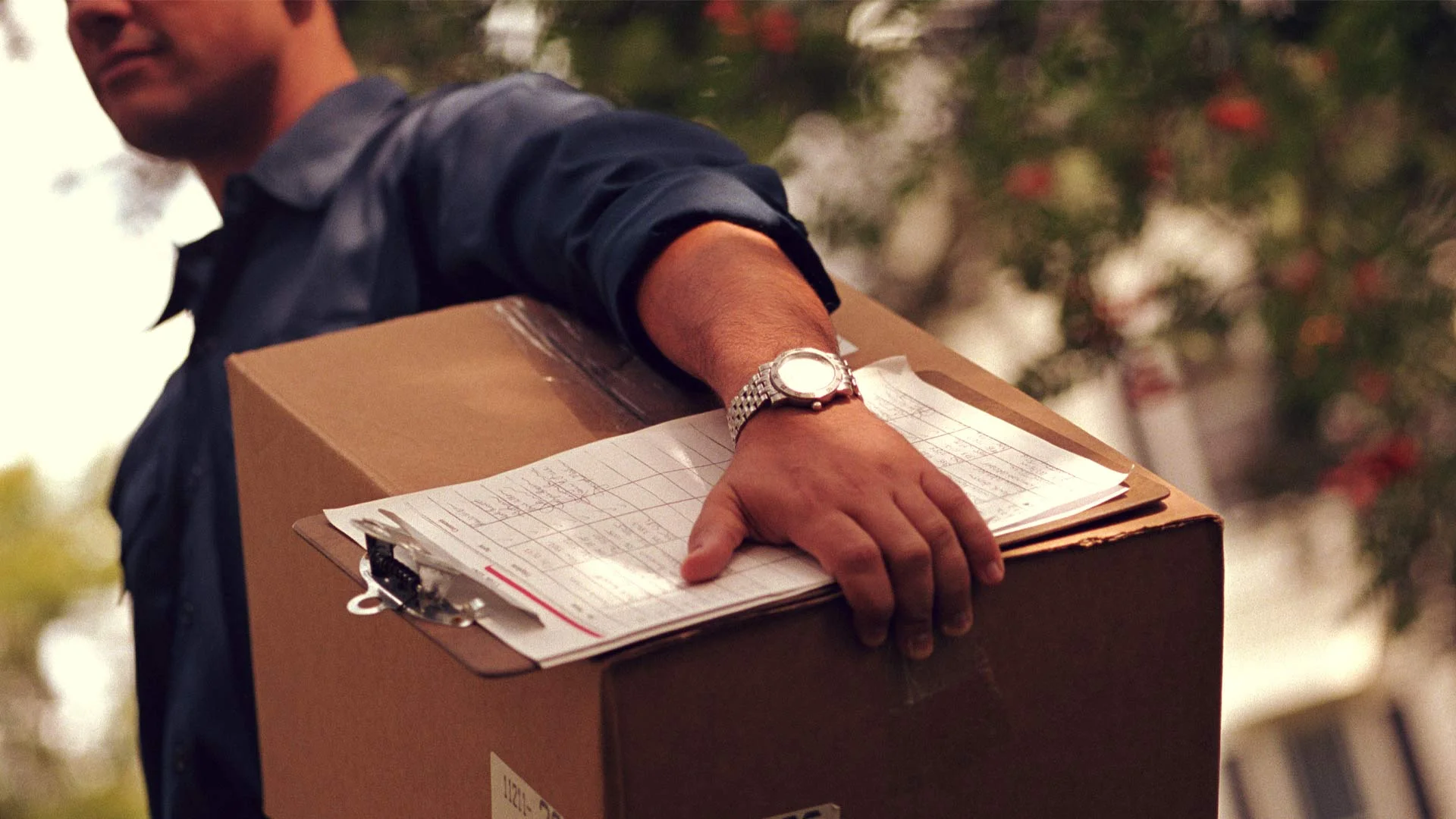 Delivery driver carrying a cardboard box and a clipboard about to deliver items that have been sold on Trade Me.